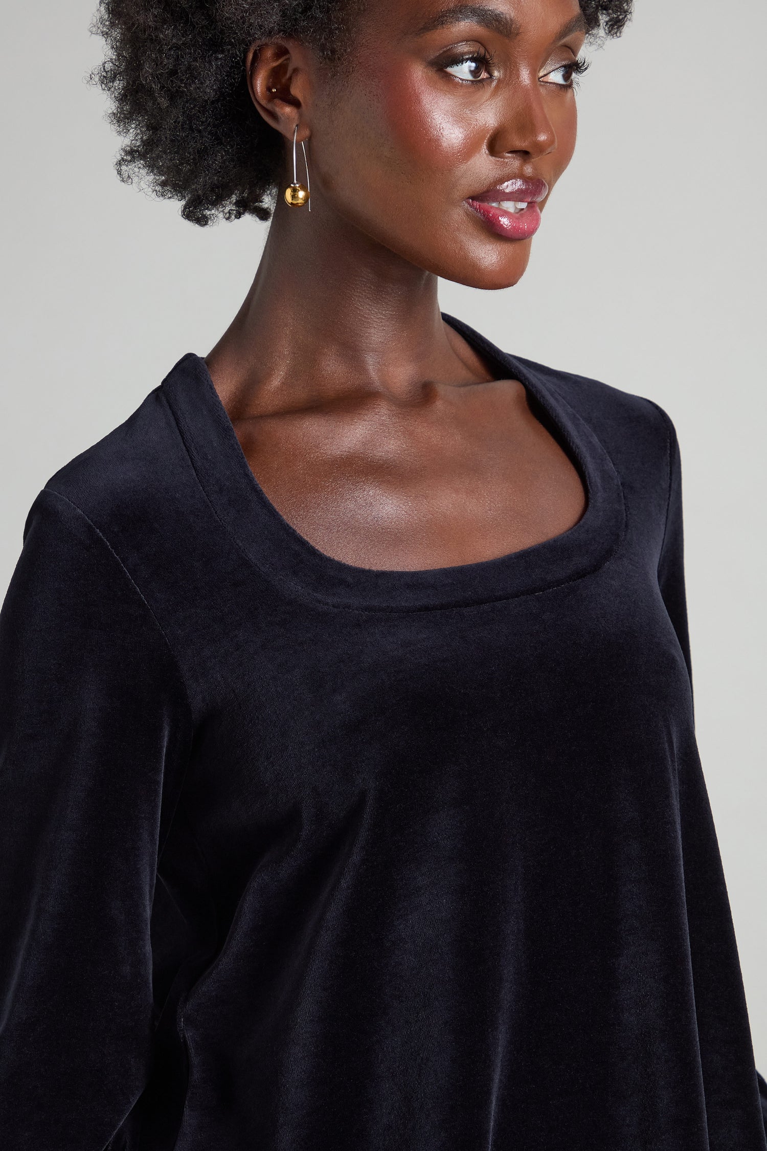A person with short curly hair and gold hoop earrings is wearing a Velvet Jersey Horseshoe Neck Top.
