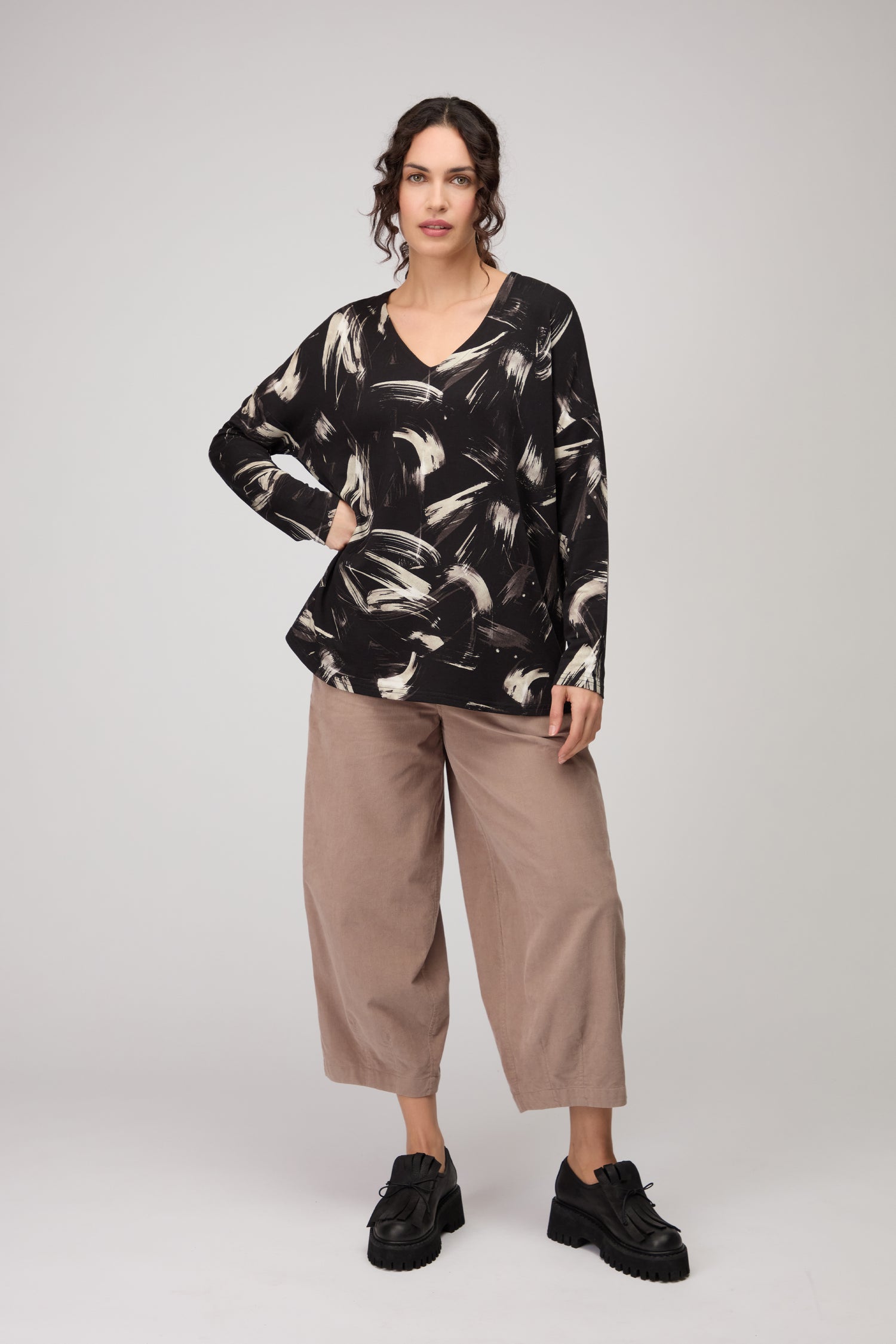 A woman stands against a plain background wearing the Painted Brushstrokes Jersey Top in black and white, paired with beige wide-leg pants and black platform shoes.