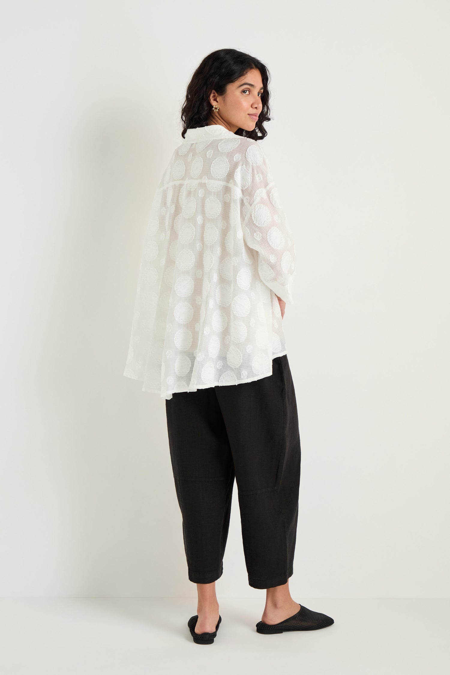 A person stands facing backward in a Jacquard Circles Shirt with an oversized fit, paired with black cropped pants and black shoes against a plain light background.