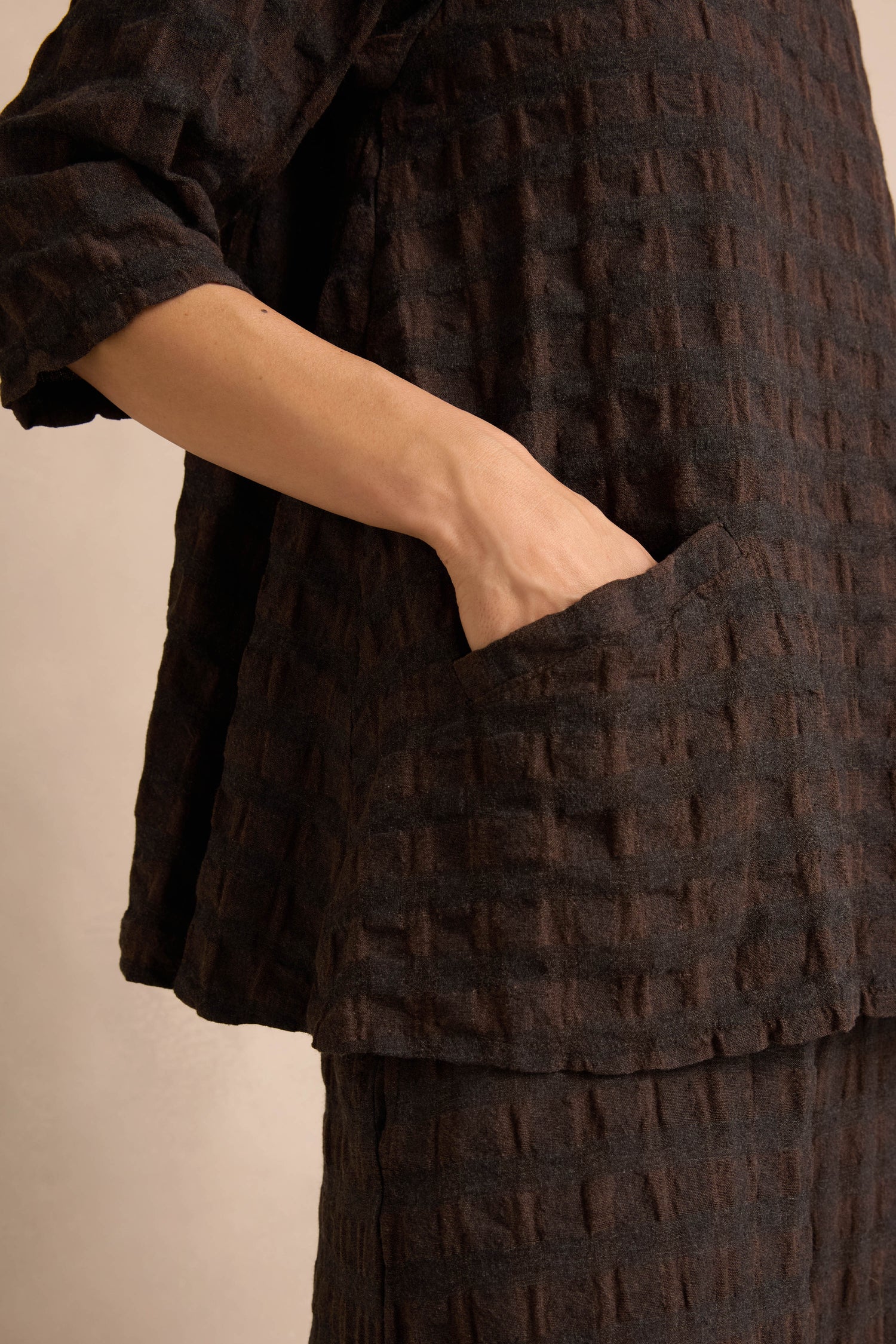 A person wearing the Chocolate Waffle Check Flared Top stands with their right hand placed inside a large front pocket.