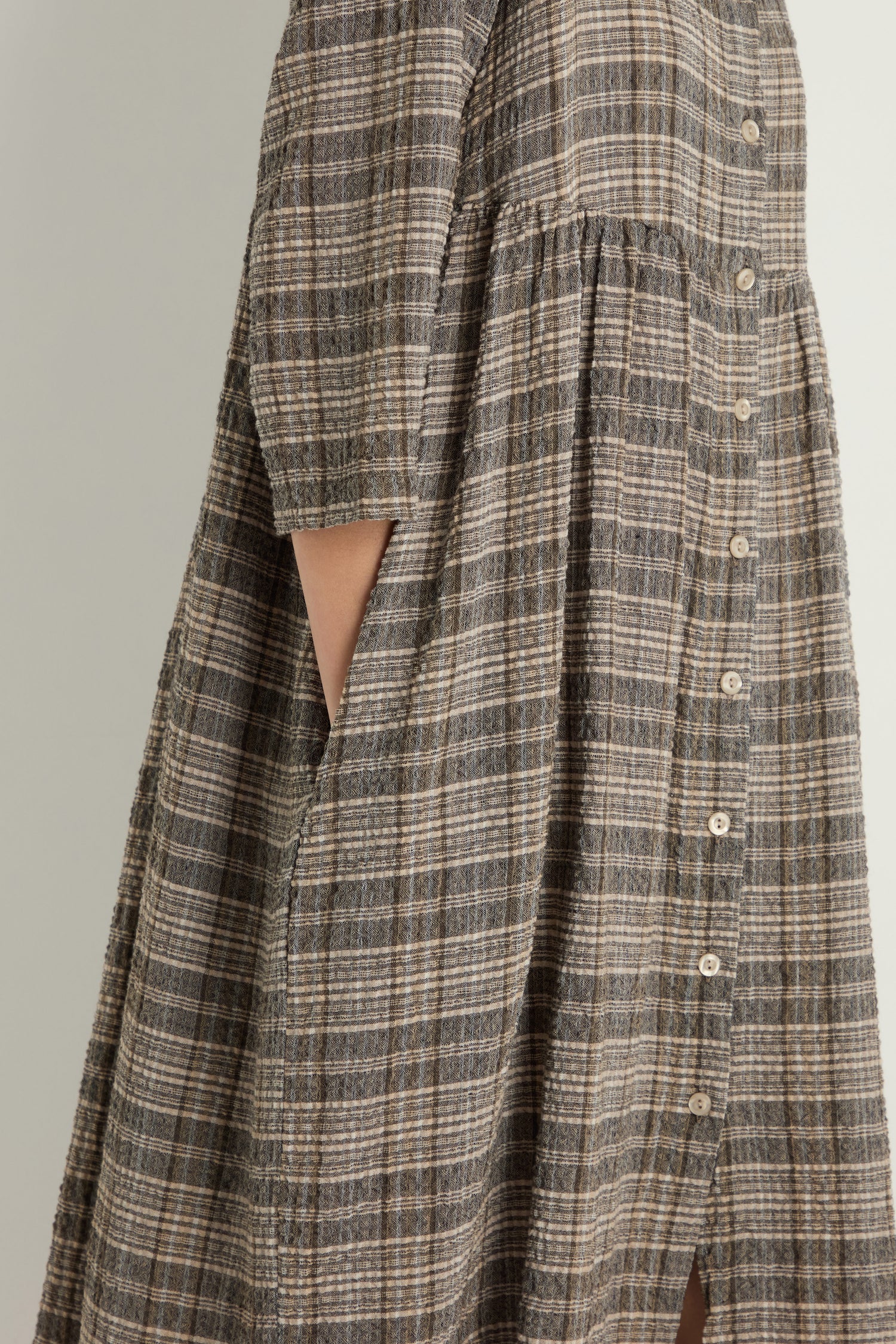 Side view of a person wearing the Check Button-Through Taupe Dress, a loose, short-sleeve textured cotton dress with pockets, highlighting Danish design.