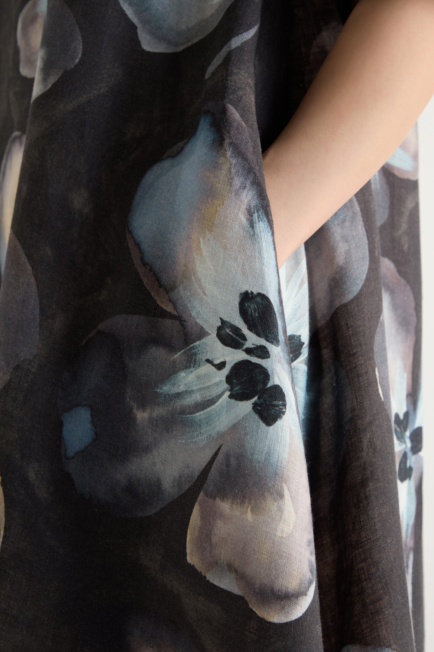 A close-up of a hand in the pocket of the Abstract Floral Linen Flared Dress, adorned with large abstract floral prints in blue, gray, and black.