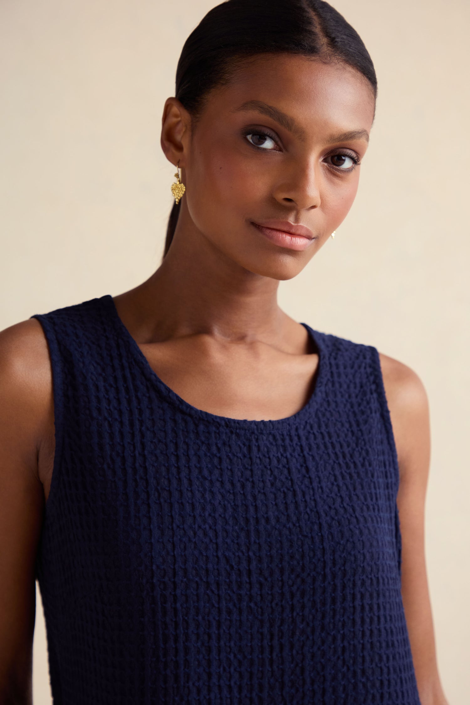 A woman with dark hair in a ponytail wears the Mini Waffle Cotton Bubble Dress and gold earrings, posing against a neutral background.