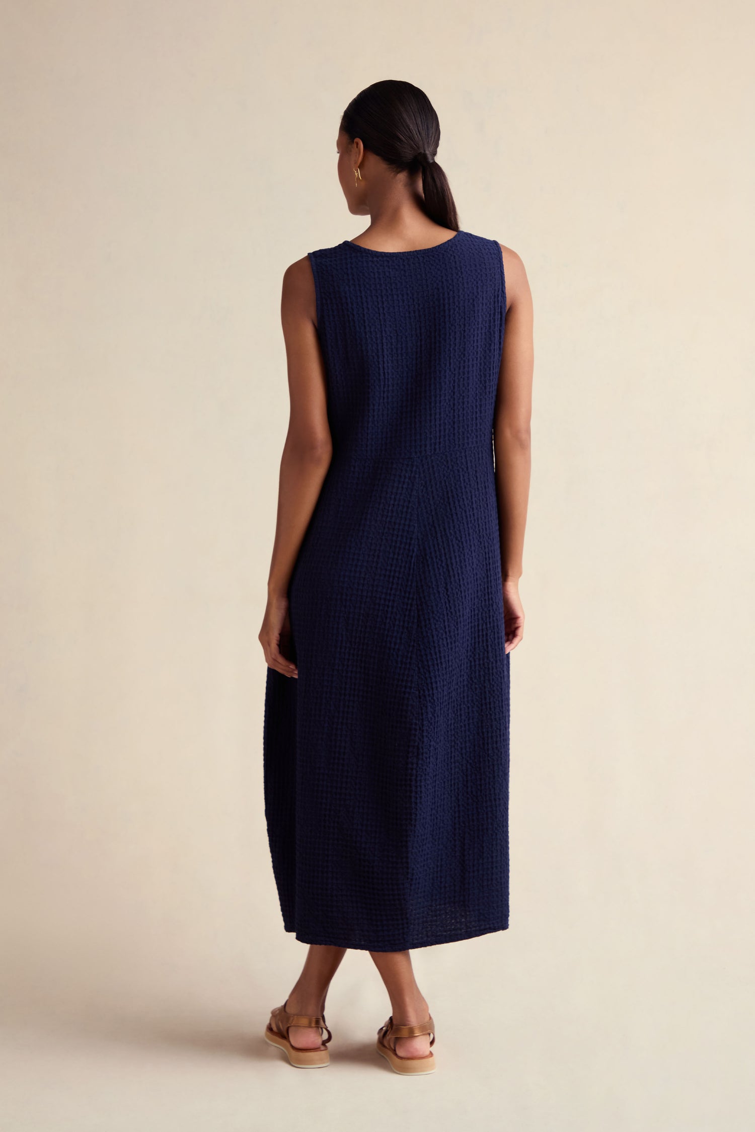 A person faces away from the camera, wearing the Mini Waffle Cotton Bubble Dress in navy blue with sandals, set against a plain light background.