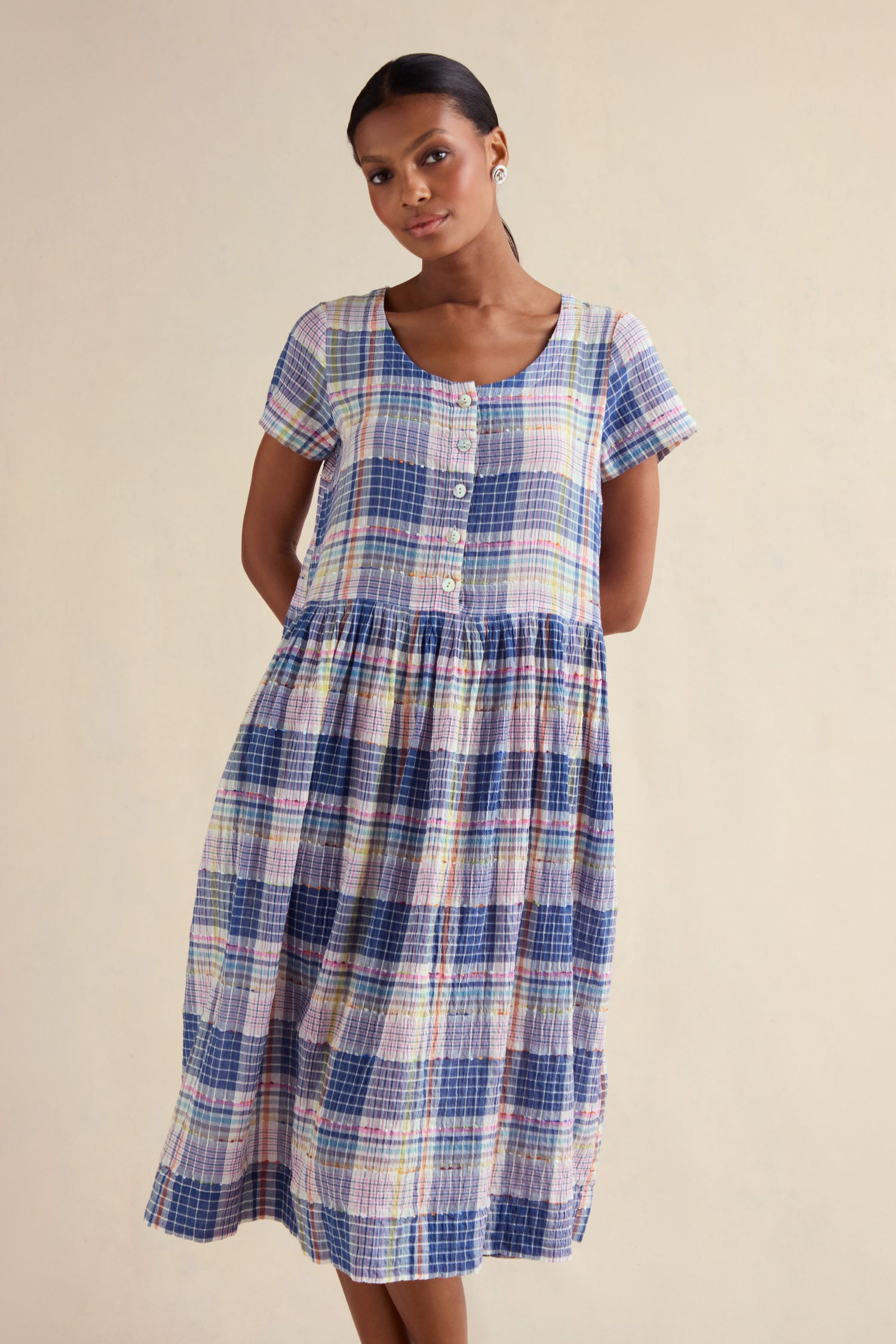 Someone wears the Crinkle Check Jacquard Dress, a short-sleeve, button-front, cotton-rich midi dress in blue, pink, and yellow plaid, standing against a plain light background.