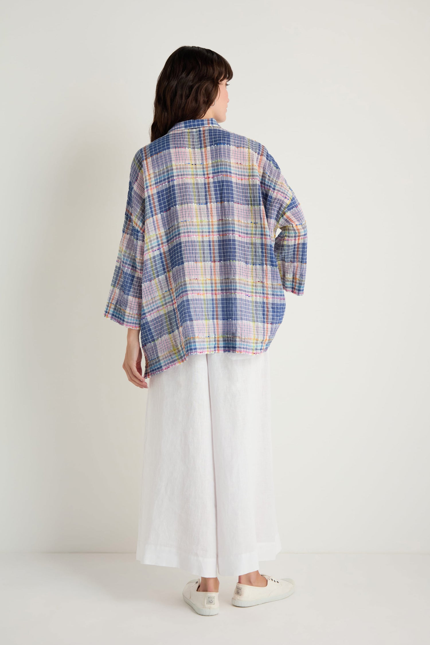 A person stands facing away, wearing the Crinkle Check Jacquard Shirt in a boxy fit with pastel colors and wide white pants, paired with white sneakers against a plain background.