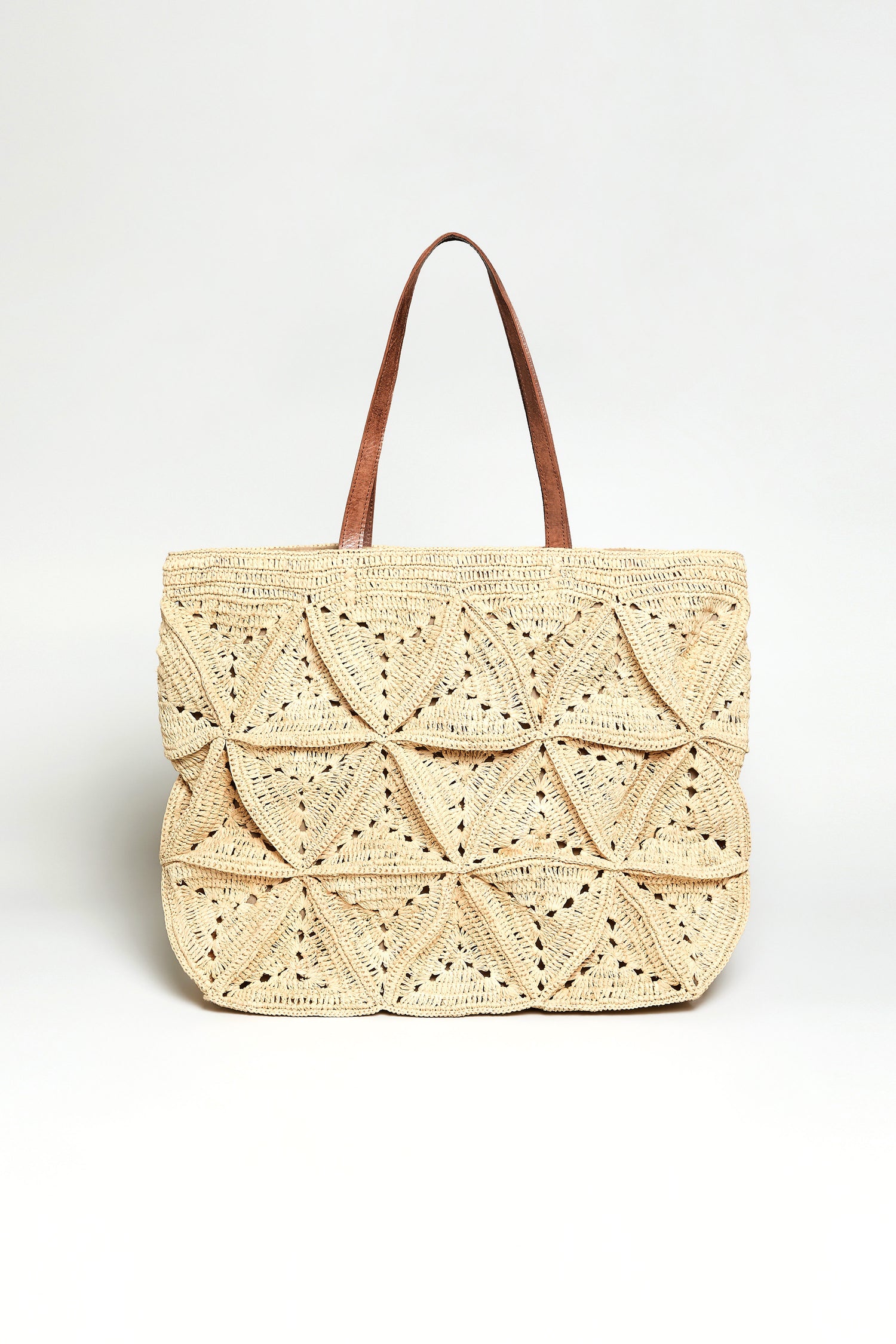 The Handwoven Raffia Basket Bag features geometric patterns and two brown handles, crafted by artisans in Madagascar. Displayed against a plain white background, it showcases intricate handwoven detail.