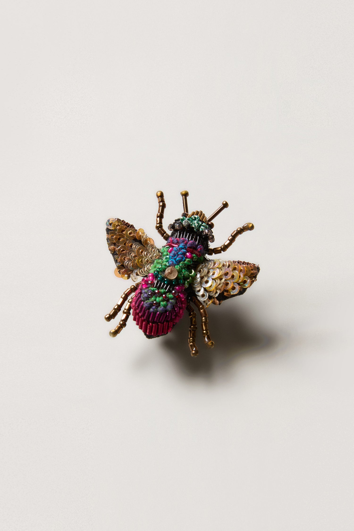 The Hand Beaded Sequin Rainbow Bee Brooch, adorned with vibrant beads and sequins, is showcased on a neutral background.