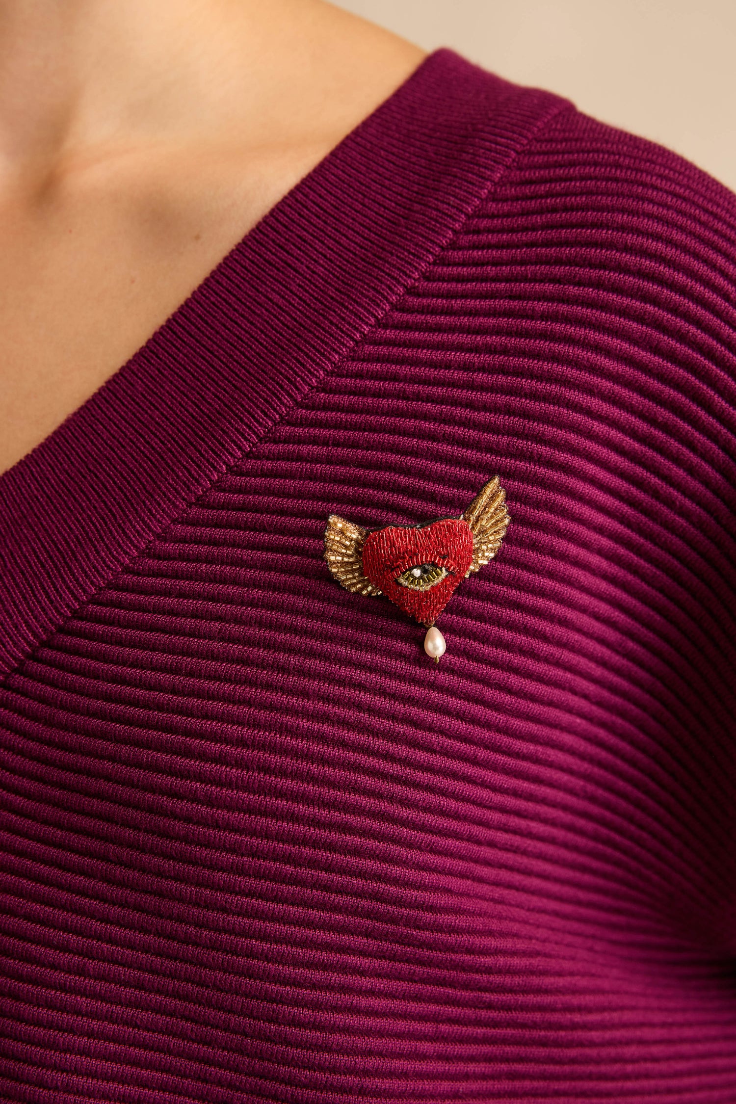 A person wearing a ribbed magenta top accessorized with the Hand Beaded Guardian Heart Brooch.