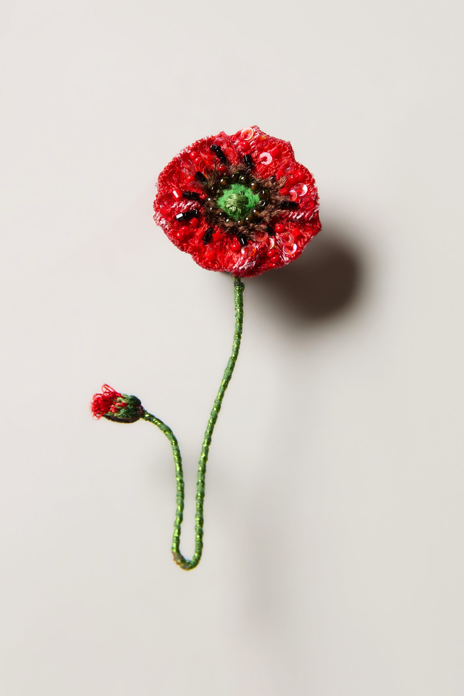 Hand Beaded Shirley Poppy Brooch featuring a red poppy with a green stem and small bud on a plain, light background—ideal for fans of botanical jewellery and handcrafted accessories.