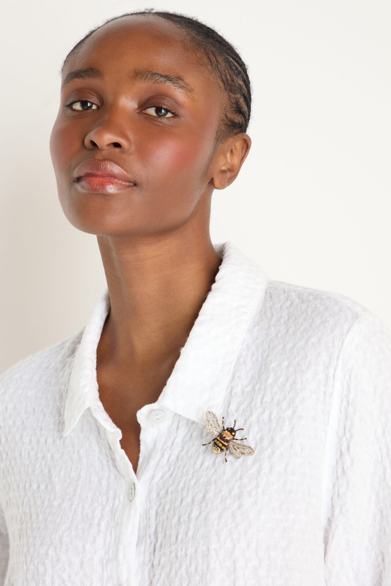 A woman wears a textured white shirt with the Hand Embroidered Humble Bee Brooch on her left side, standing against a plain light background.