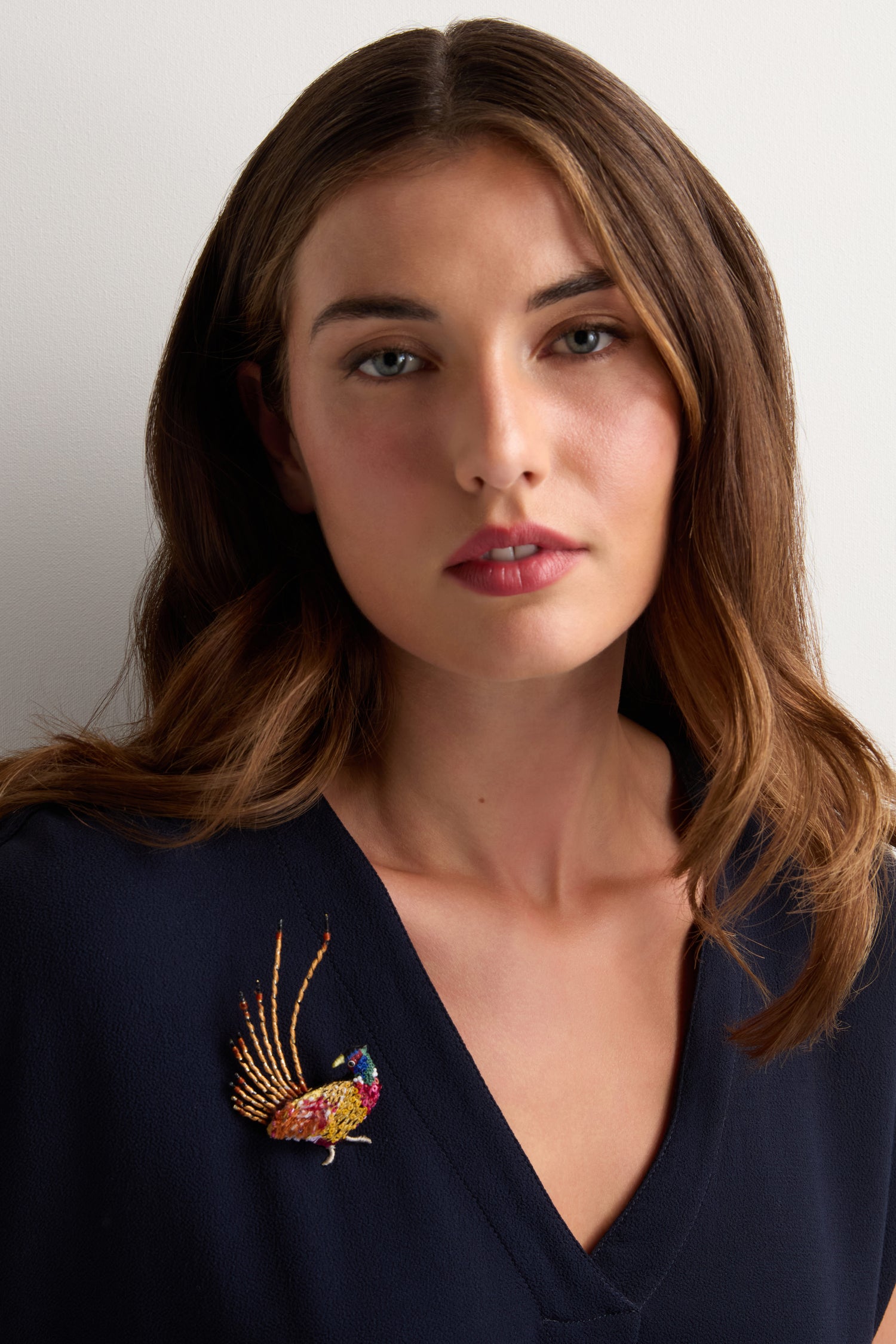 A woman with brown hair, dressed in a navy blue top, showcases the Hand Beaded Pheasant Brooch against a plain light background.