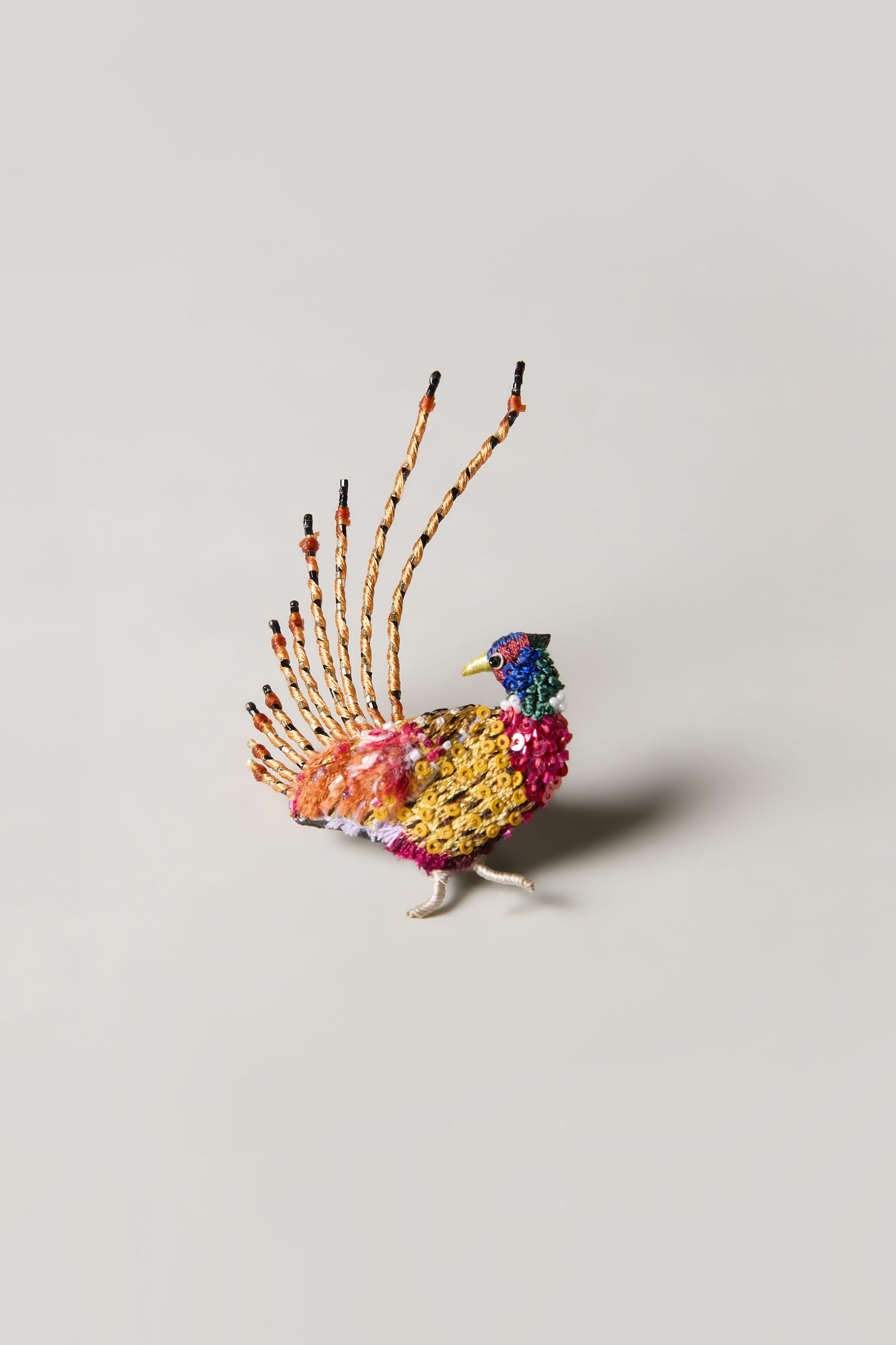 The Hand Beaded Pheasant Brooch, featuring vibrant beads and an upright, fan-like tail, is shown against a simple light background—a perfect gift for nature lovers.