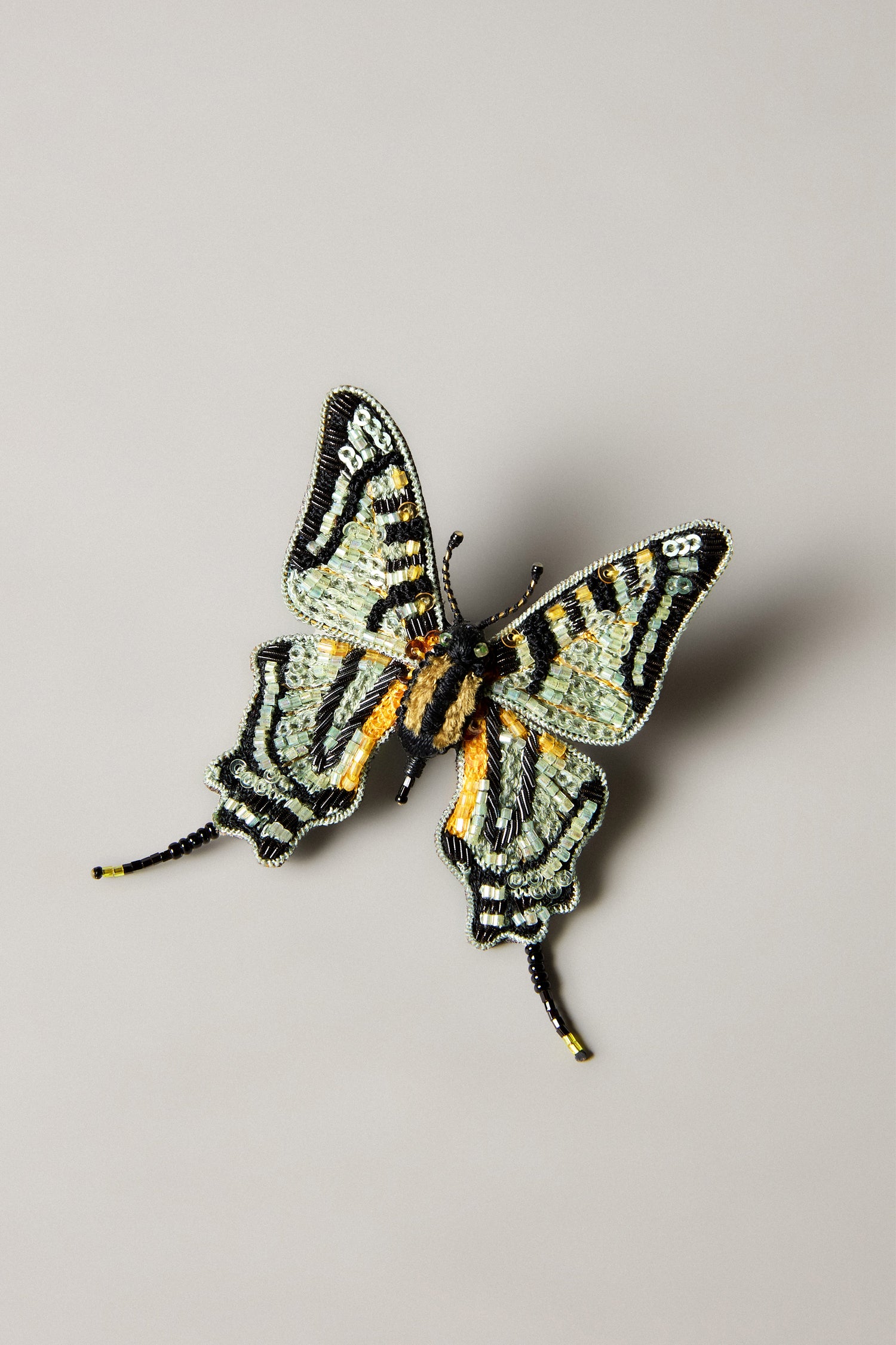 This Hand Beaded Swallowtail Brooch by Trovelore is an embroidered accessory featuring black, yellow, and light blue beading on a plain light gray background.