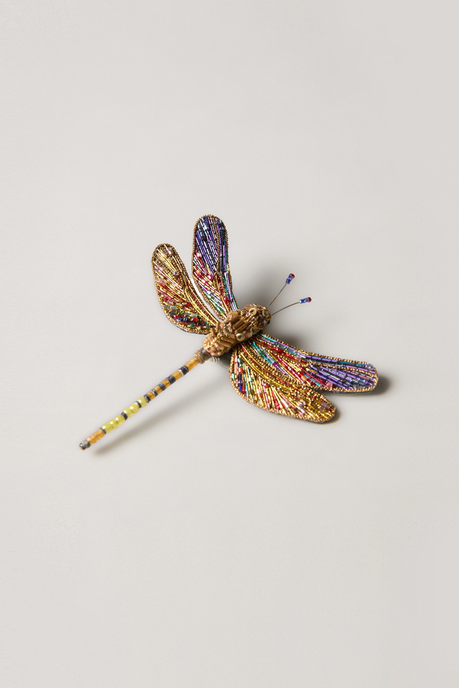 The Hand Beaded Hawker Dragonfly Brooch showcases multicolored beads and detailed hand-stitched wirework on a neutral base—an eye-catching piece of wearable art.