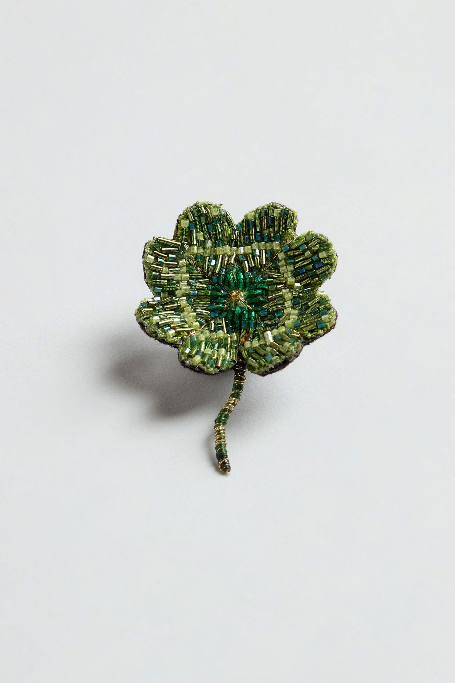 The Hand Beaded Vintage Clover Brooch features a decorative four-leaf clover crafted from small green beads with a beaded stem, evoking the charm of a classic clover pin, displayed against a simple light background.