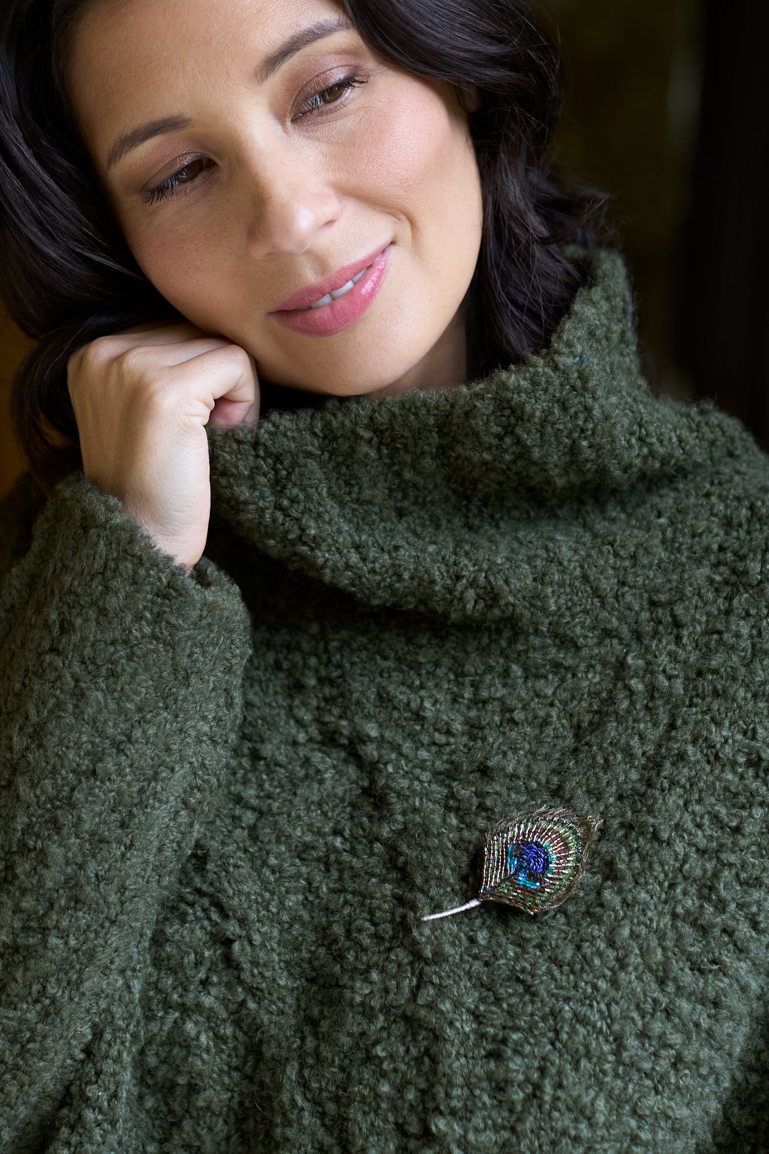 A woman in a textured green turtleneck sweater wearing the Hand Beaded Peacock Feather Brooch.
