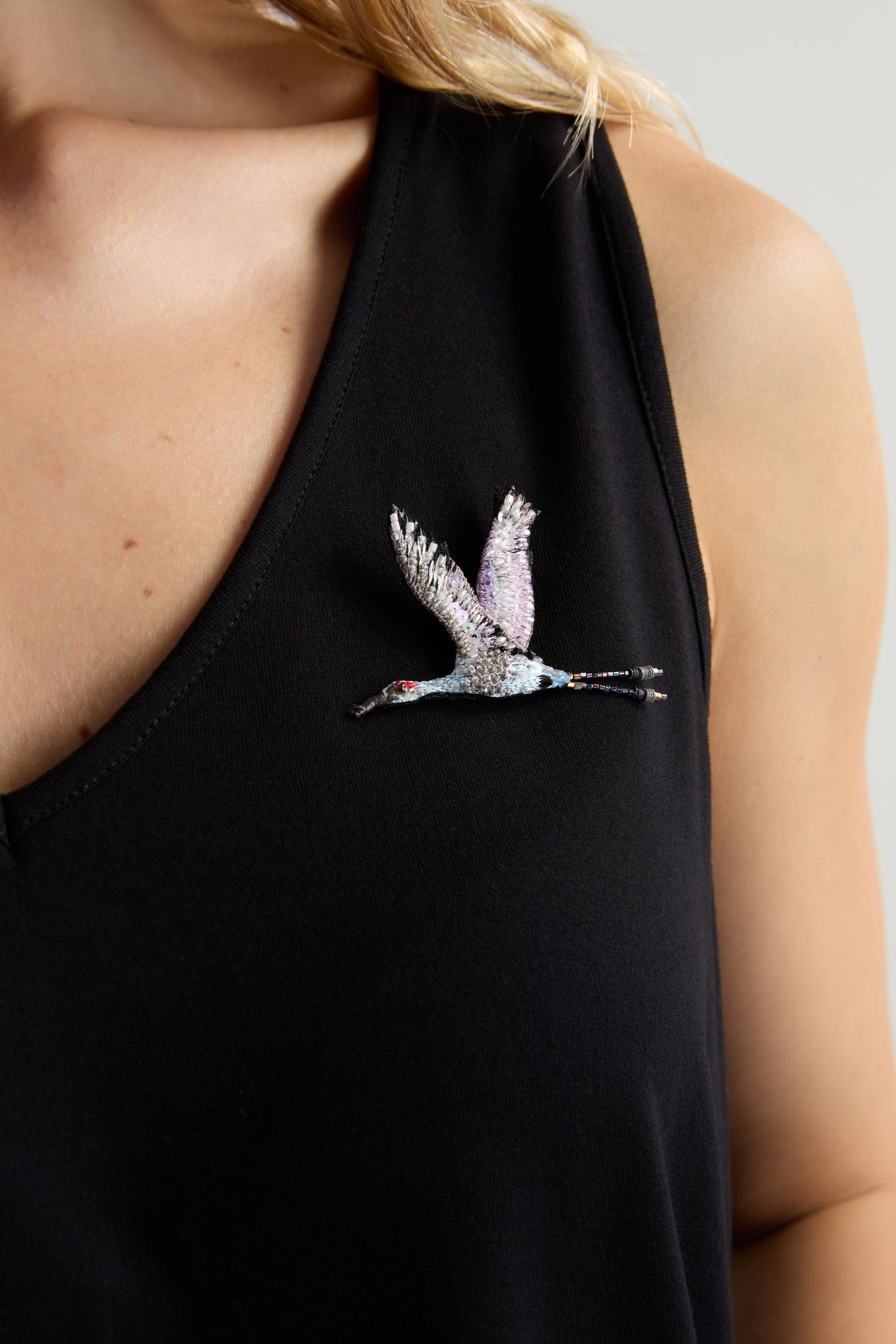 A person wearing a black sleeveless top with a Hand Beaded Sandhill Crane Brooch, metallic and bird-shaped, pinned on the left side of the chest.