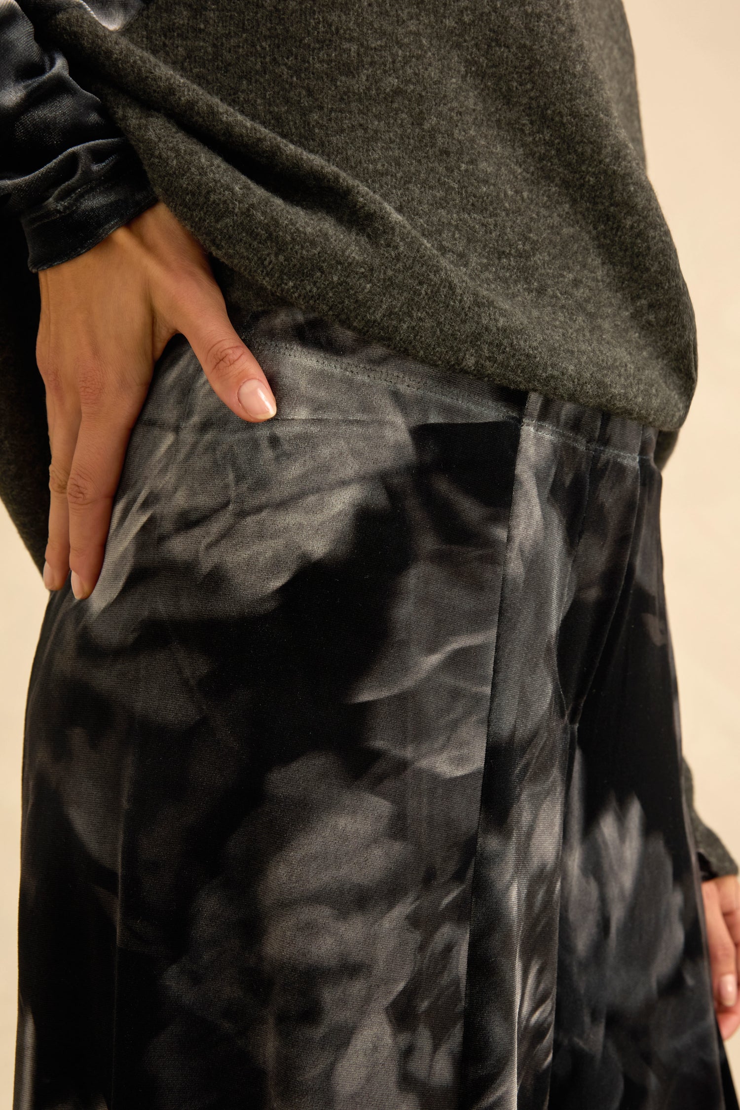 Wearing a dark grey sweater and the Blurred Floral Velvet Bubble Trousers, which feature sculptural volume, a person rests their hand on their hip.