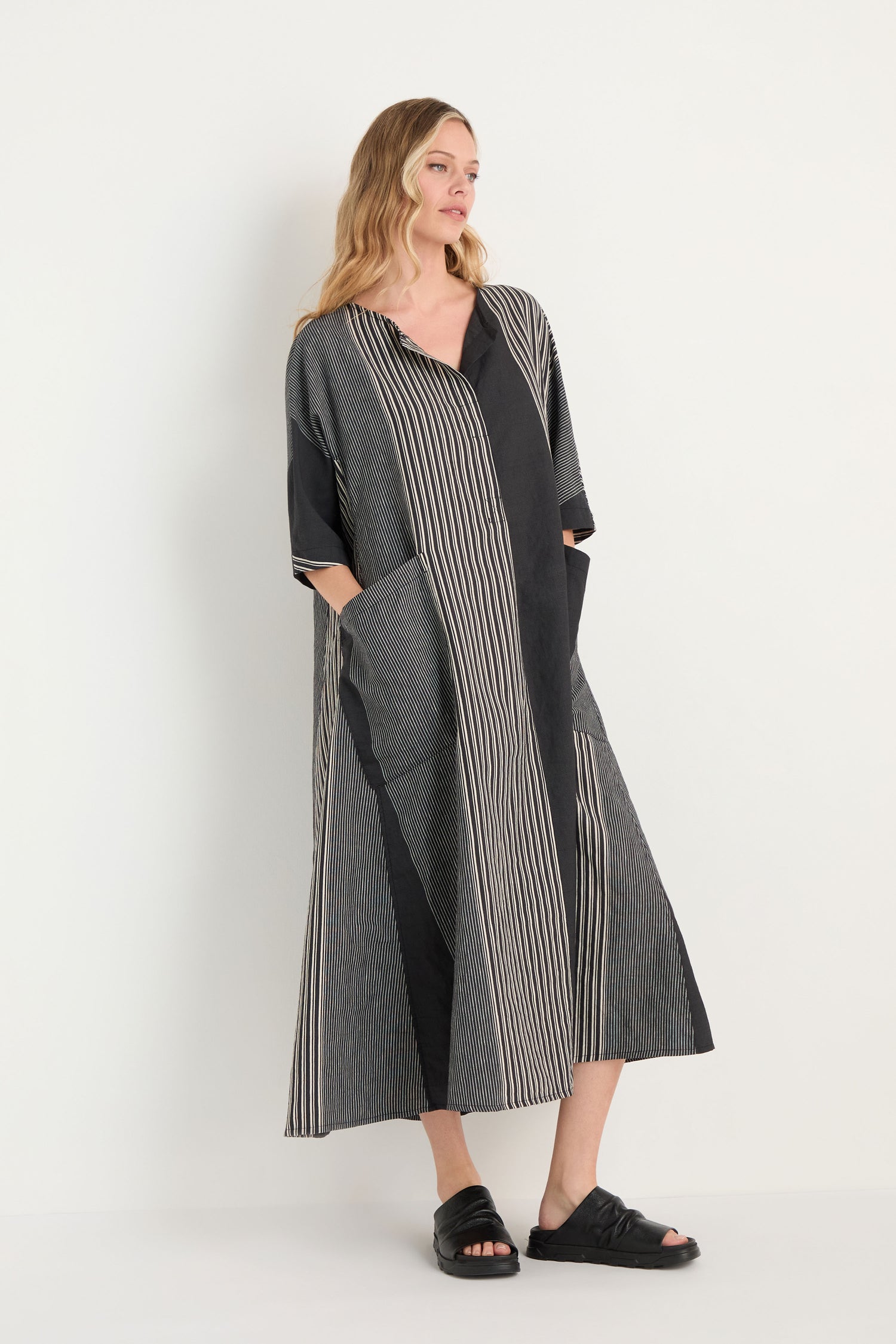 A woman with long curly hair wears the Mixed Stripe Easy Dress—featuring black and white vertical and diagonal stripes—while standing against a plain light background.