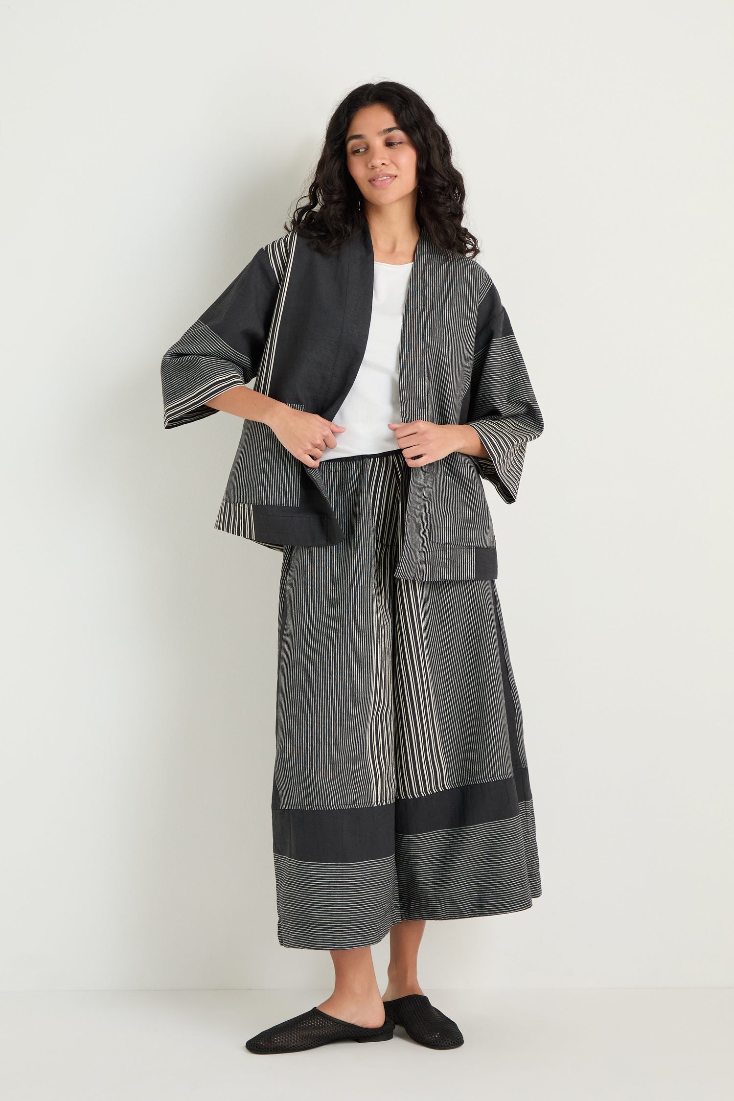 A person stands against a white wall wearing the Mixed Stripe Easy Jacket with matching wide-leg pants, a white top, and black slip-on shoes.