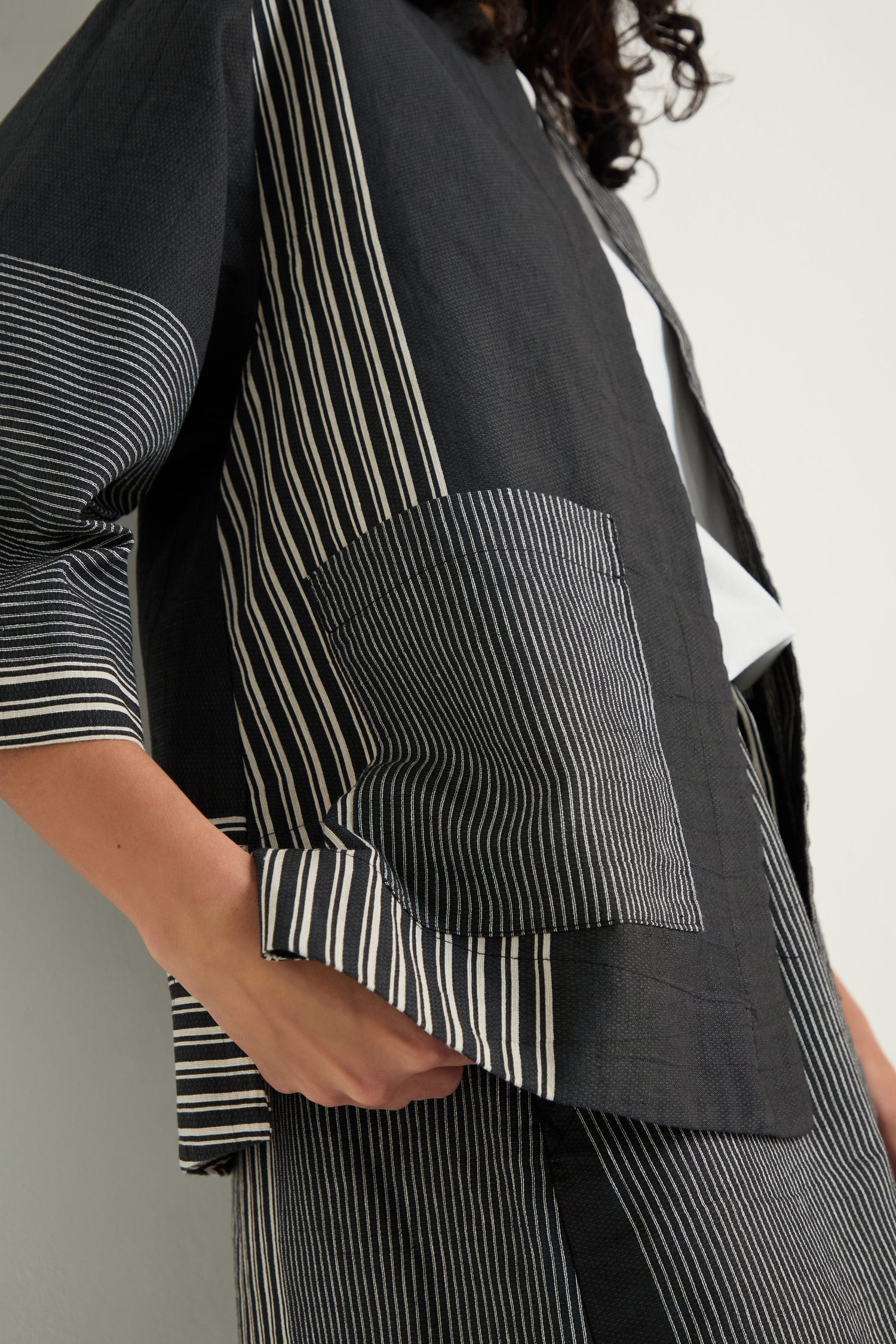 A person wearing the Mixed Stripe Easy Jacket, a relaxed boxy style with large front pockets and black-and-white stripes, paired with a matching skirt, stands against a light background.