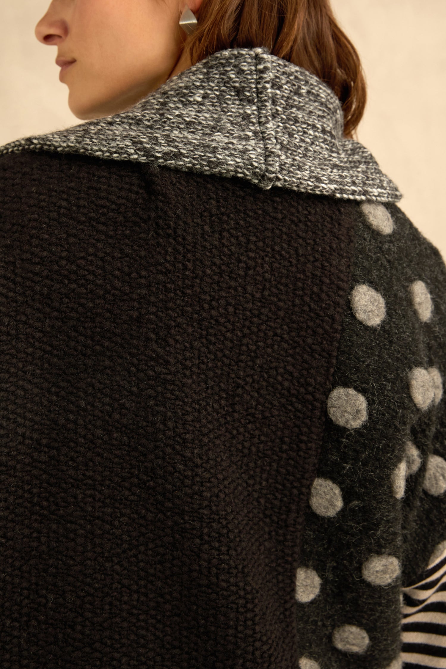 A person is shown from the back wearing the Mixed Spot Stripe Cardigan, featuring a patchwork of textured black knit with a gray collar, polka dot sleeve, and striped detailing.