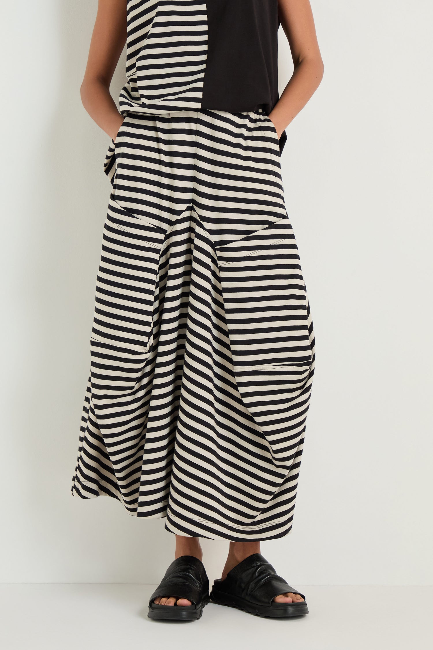 Model wears Stripe Balloon Trousers with a matching top and black sandals, standing against a plain white background for a chic, modern look.