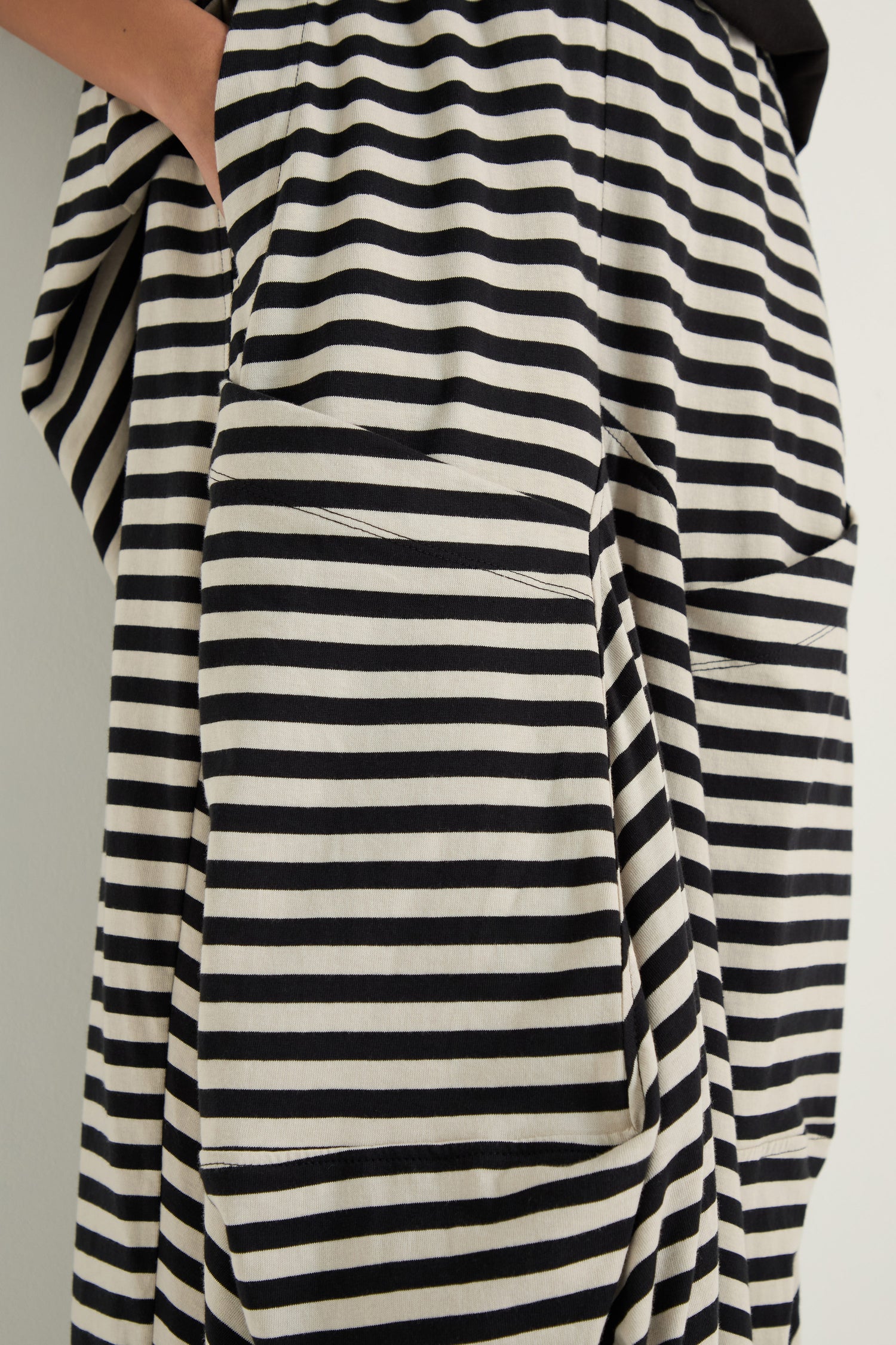 Close-up of a person wearing Stripe Balloon Trousers—black and white cotton striped pants with large front pockets; one hand rests partially in a pocket.