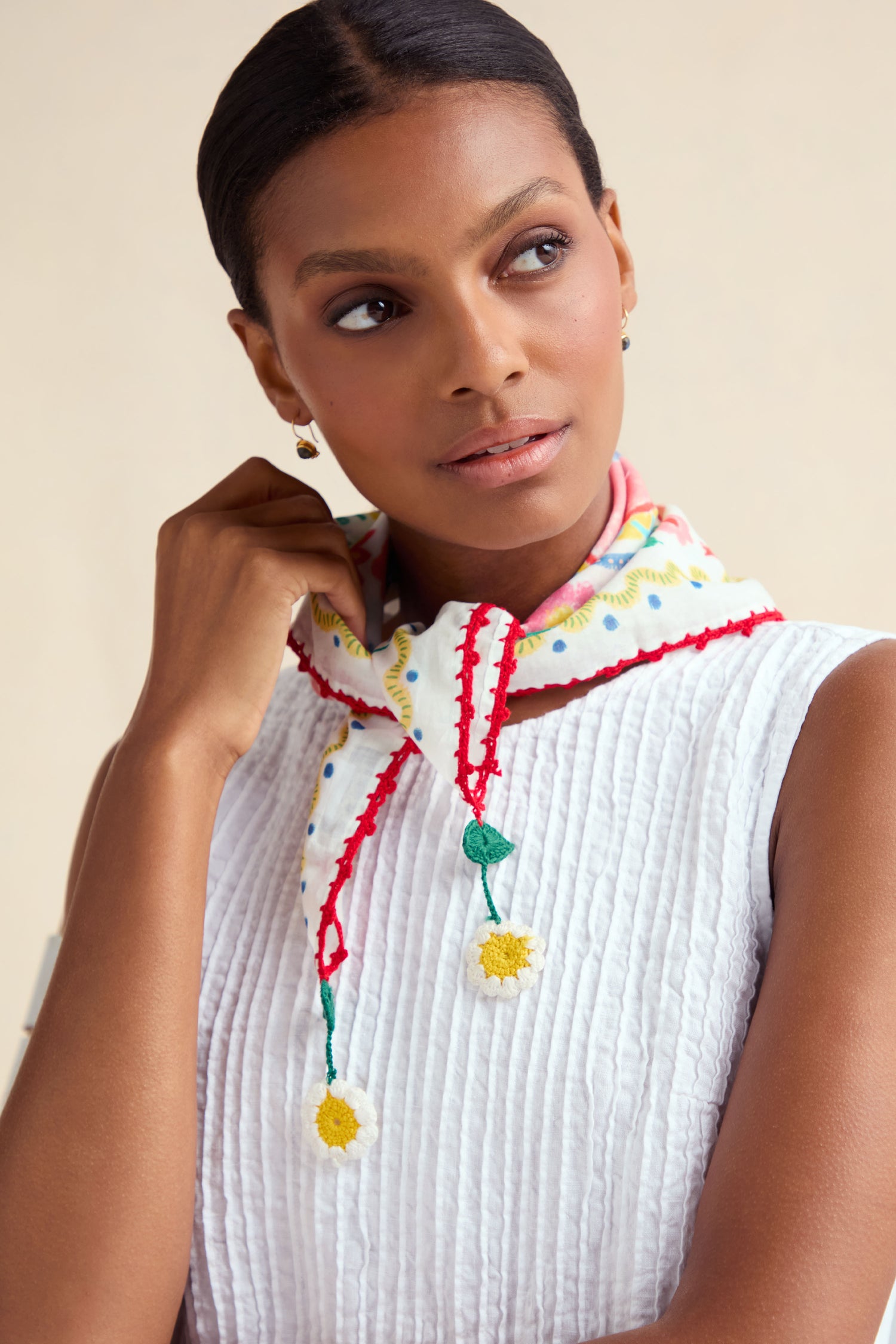 Woman wearing a white textured sleeveless top and the Embroidered Love In Bloom Cotton Bandana, featuring red trim and yellow flower accents, looking slightly to the side.
