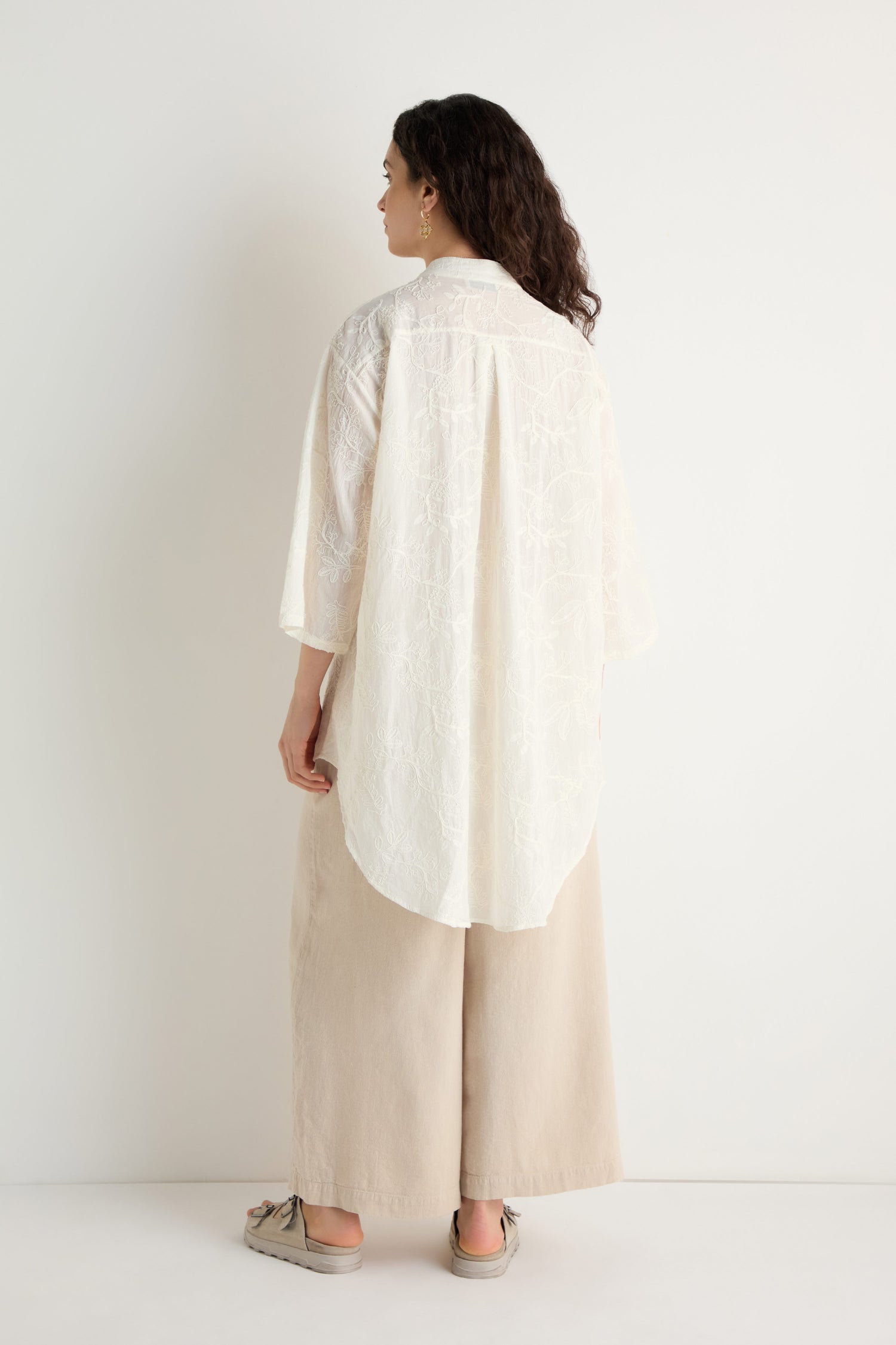 A person faces away, wearing the Embroidered Long Floral Shirt paired with wide beige pants and beige shoes, set against a plain white background.