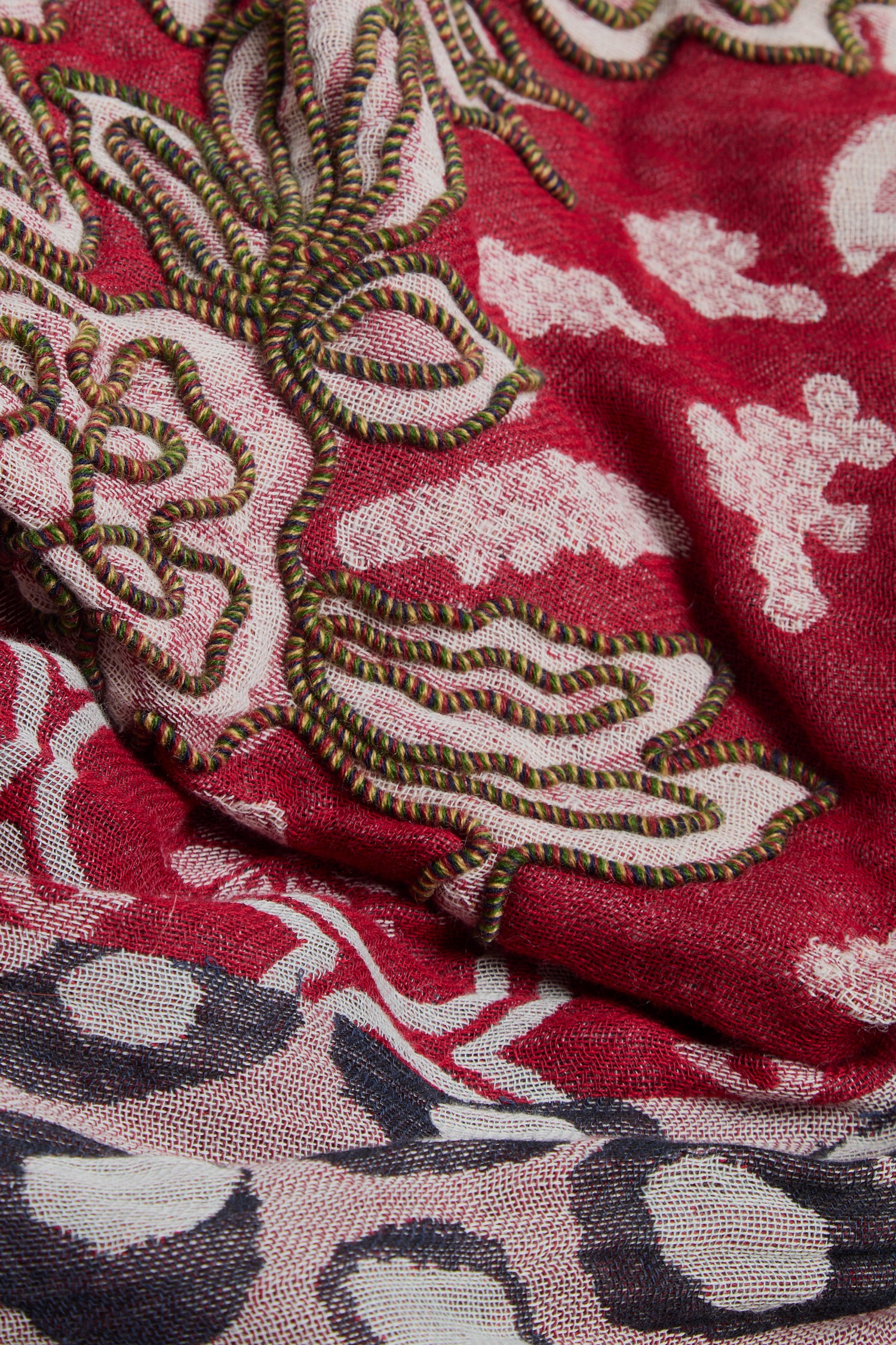 Close-up of the Embroidered Cotton Wool Scarf, showcasing vivid red fabric adorned with intricate green, white, and black embroidery in geometric floral motifs and abstract patterns. This beautiful scarf is elegantly finished with delicate fringed edges.