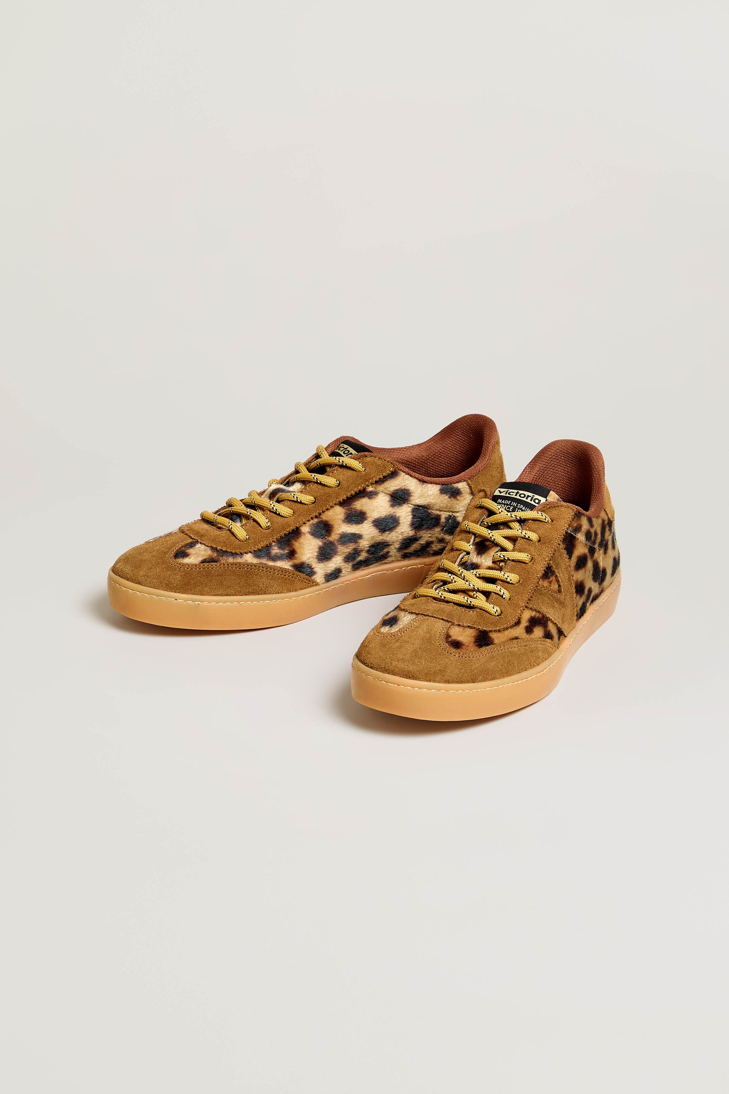 A pair of Berlin Animal Print Trainers featuring tan soles, brown suede accents, yellow laces, and a leopard print pattern on the sides, crafted in Spain and shown against a plain light background.