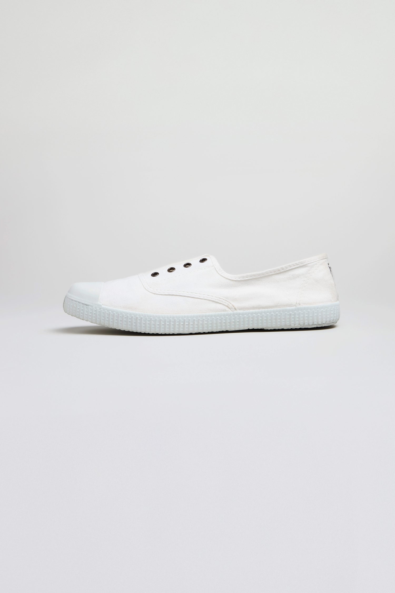The Inglesa White Pumps, classic trainers made from recycled DREC cotton with a rubber sole and four eyelets, are shown in profile against a light gray background.