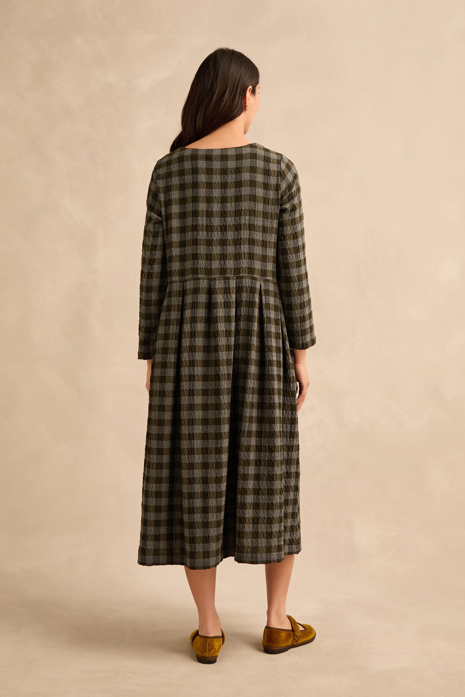 A person stands with their back to the camera, wearing the Crinkle Check Flared Dress and brown flat shoes against a plain beige background.
