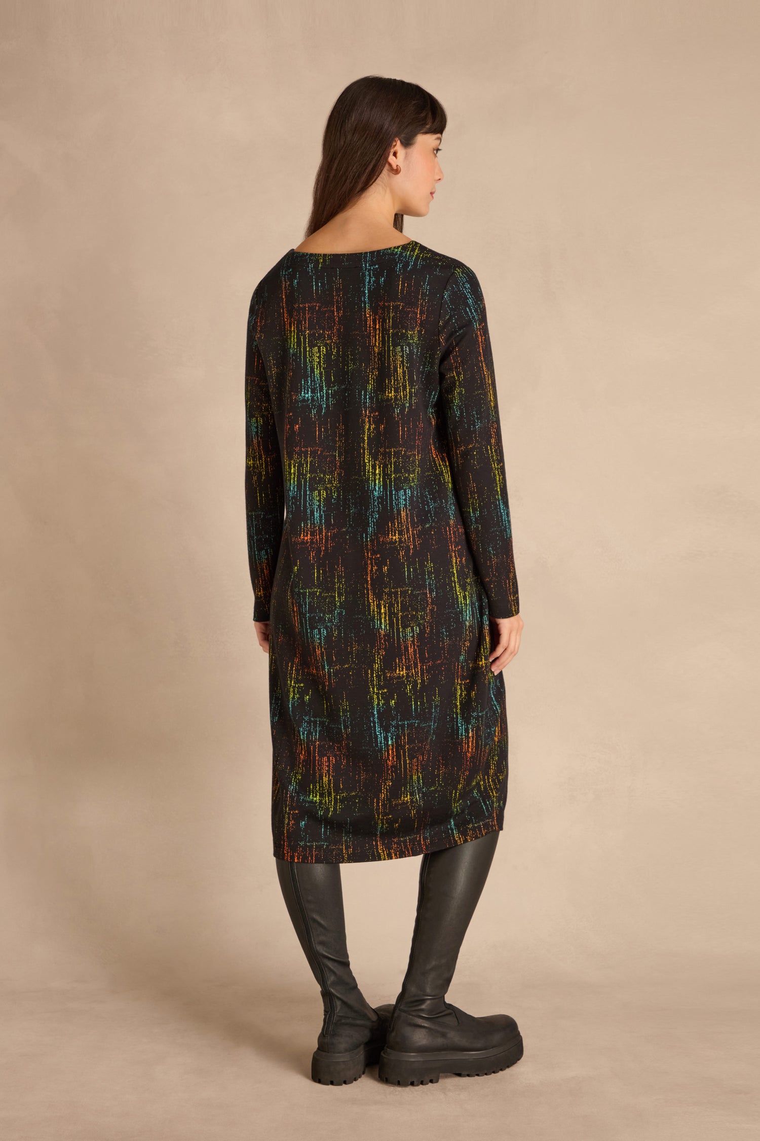 Woman stands with her back to the camera, wearing the Space Dye Jacquard Jersey Dress and black knee-high boots.