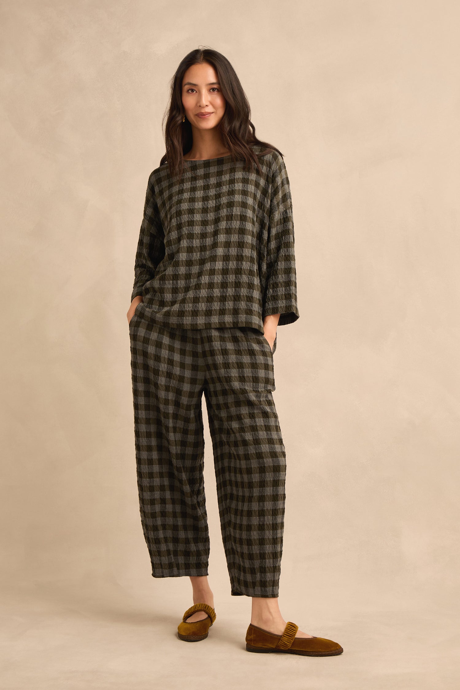 A woman stands facing forward with her hands in her pockets, wearing the Crinkle Check Boxy Top and matching pants, styled with brown loafers against a neutral beige background.