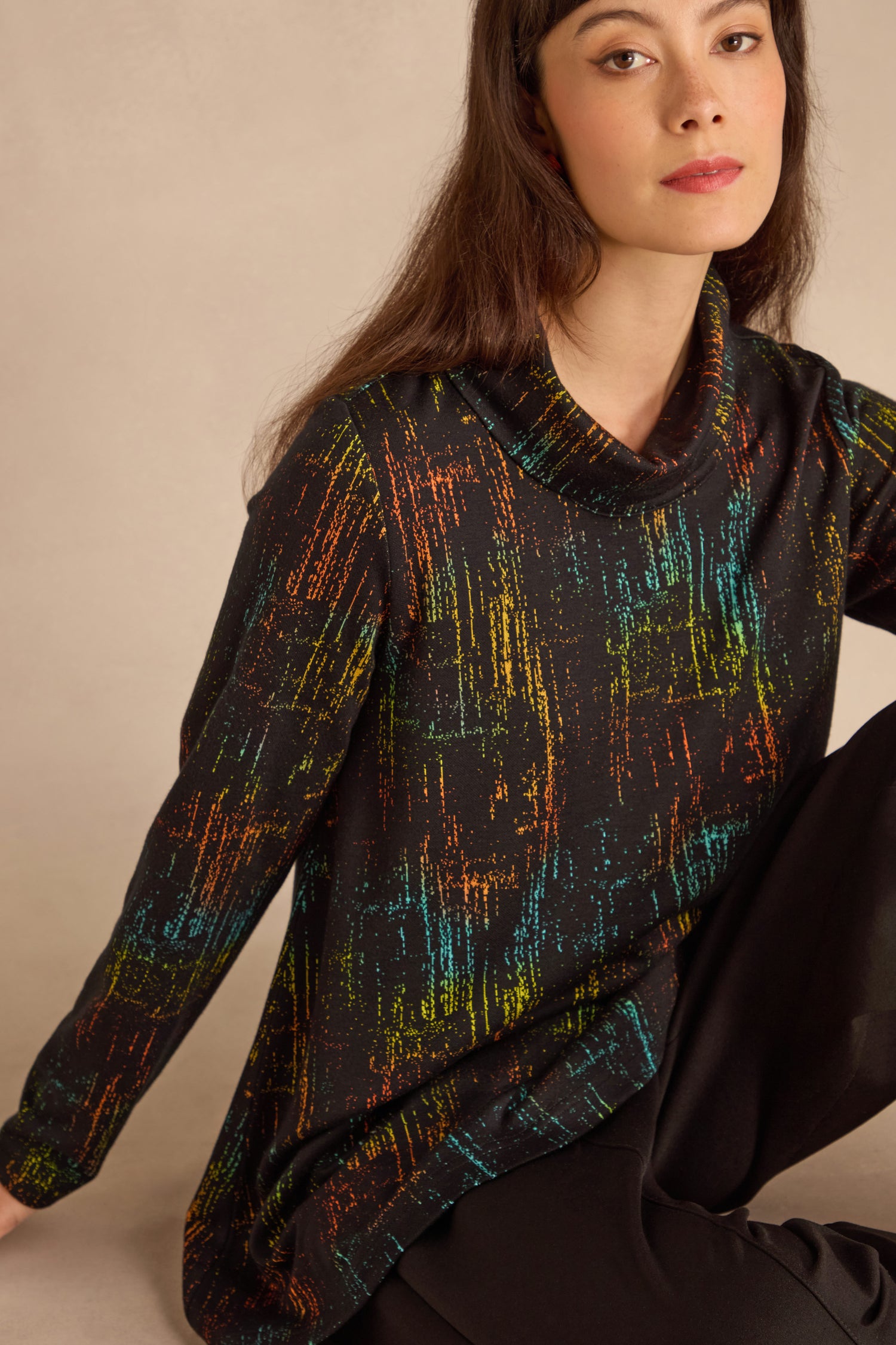 A woman with long brown hair wears the Space Dye Jacquard Jersey Tunic and black pants, seated against a neutral background.