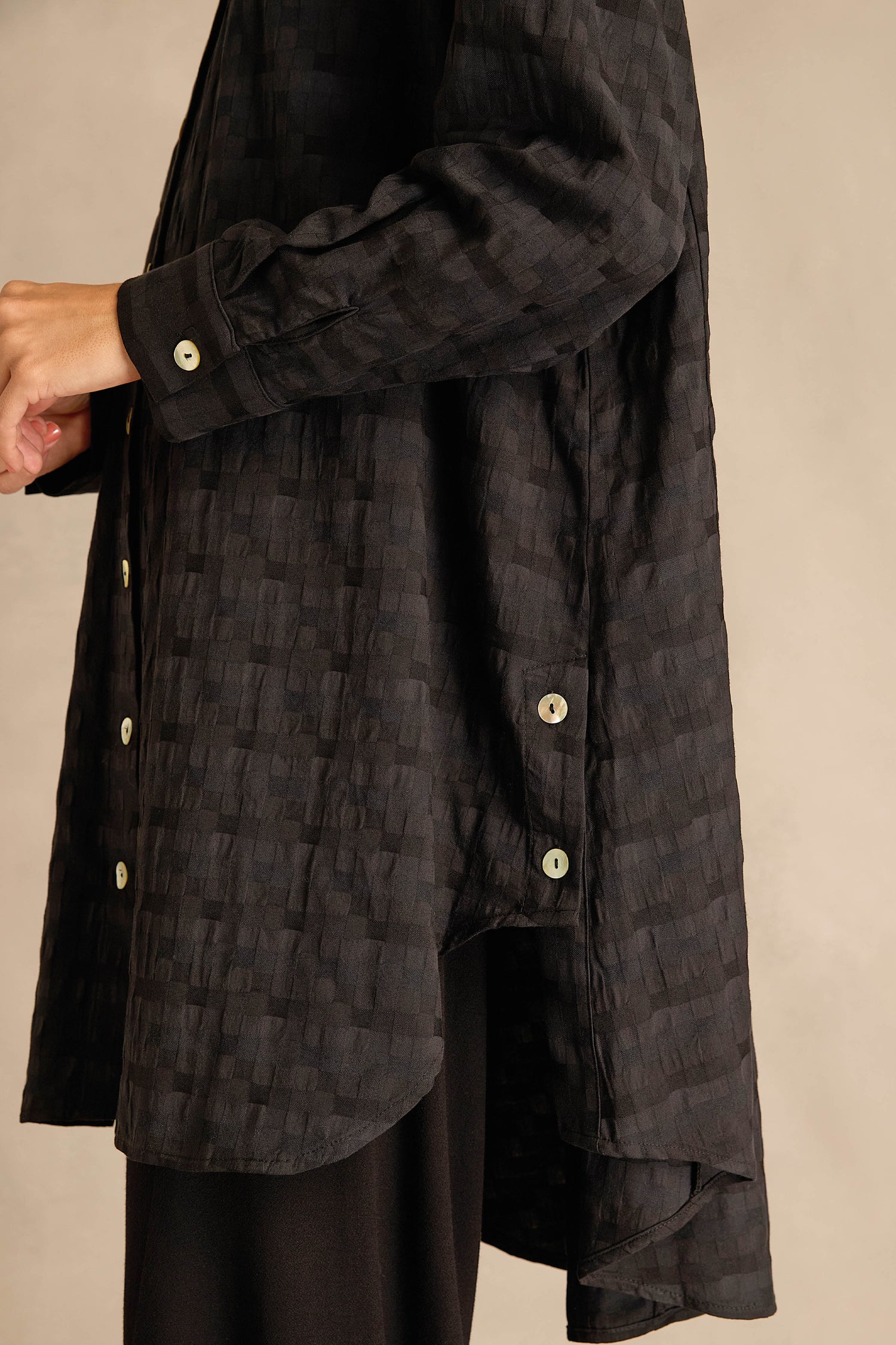 Person wearing the Jacquard Squares Long Line Shirt, a textured black shirt with side and front buttons, shown from the shoulder to mid-thigh against a neutral background.