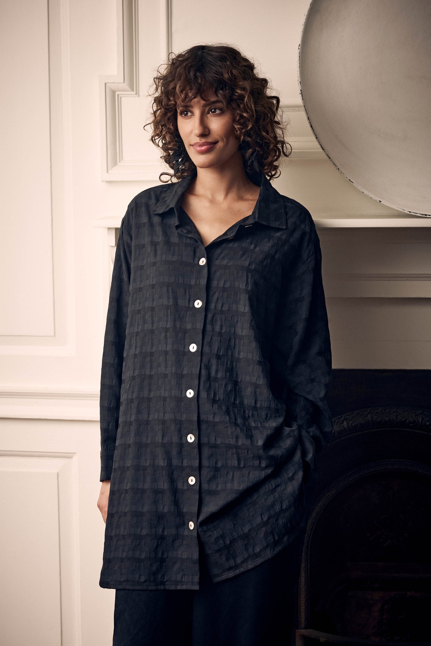 A woman wears a black Jacquard Squares Long Line Shirt featuring a textured, tonal jacquard square pattern.