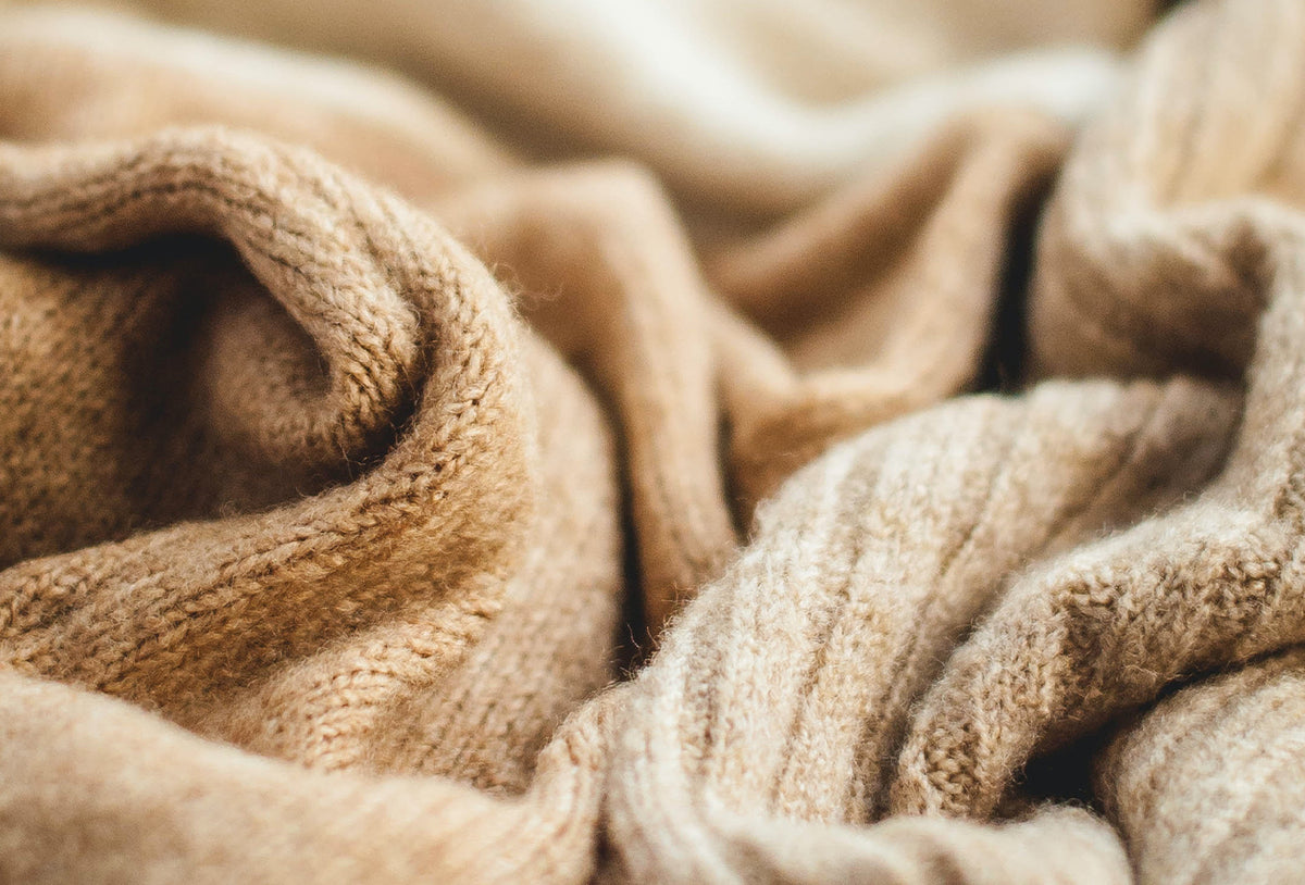 A image of a wool fabric in warm beige tones is draped and folded, showcasing a textured knit pattern.