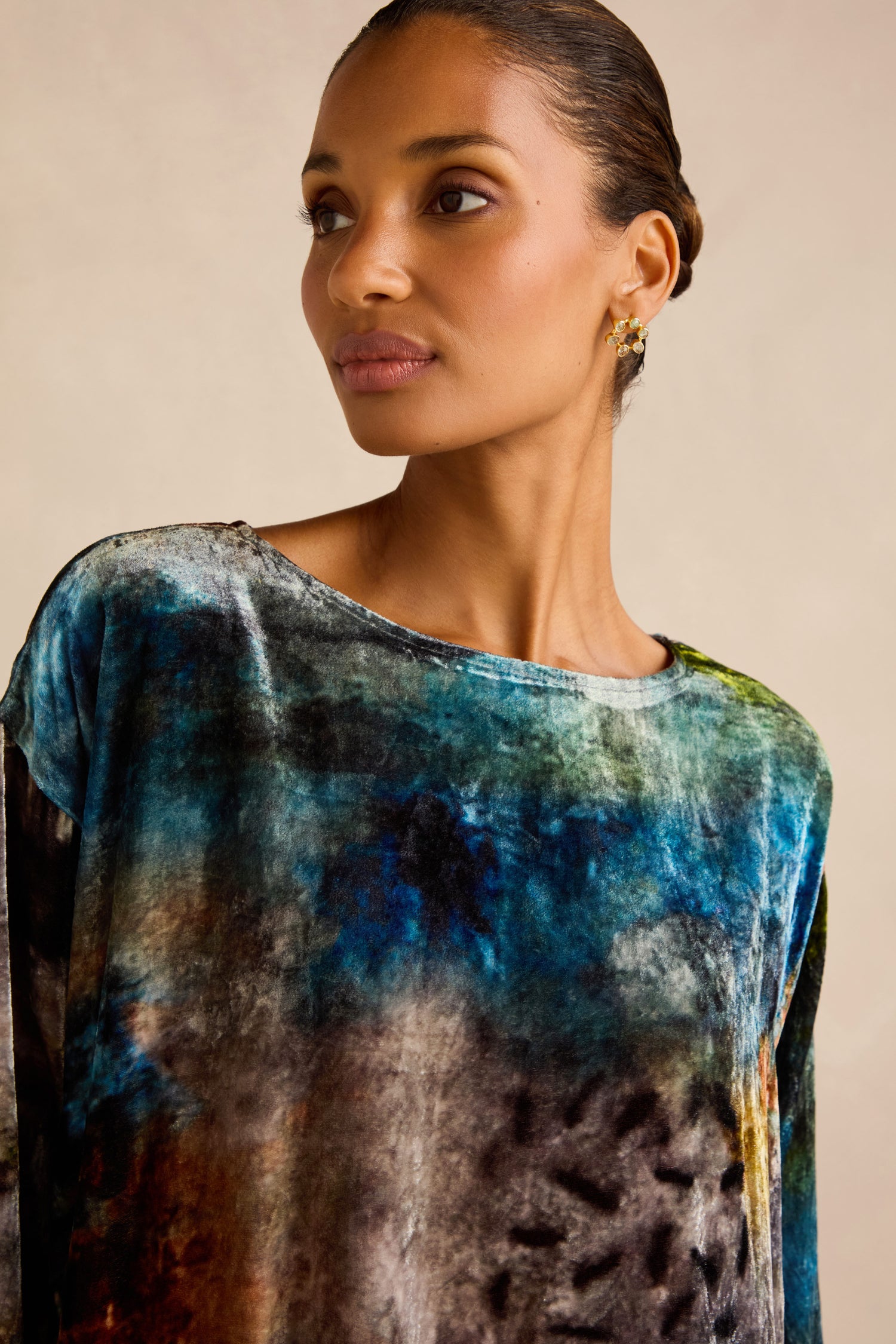 A woman wearing the Sunset Silk Velvet Tunic—featuring a multicolored, abstract pattern in an exclusive artisan-crafted print—looks slightly to the side against a neutral background.