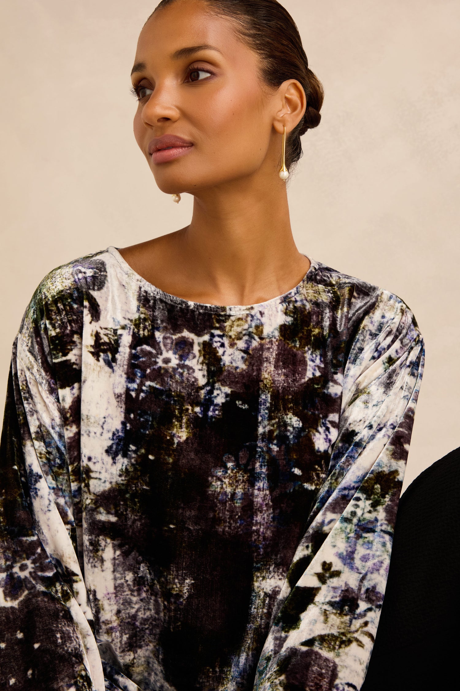 A woman wearing the Printed Silk Velvet Top, featuring an artisan-made floral design, and gold drop earrings, sits against a neutral background looking slightly to the side.