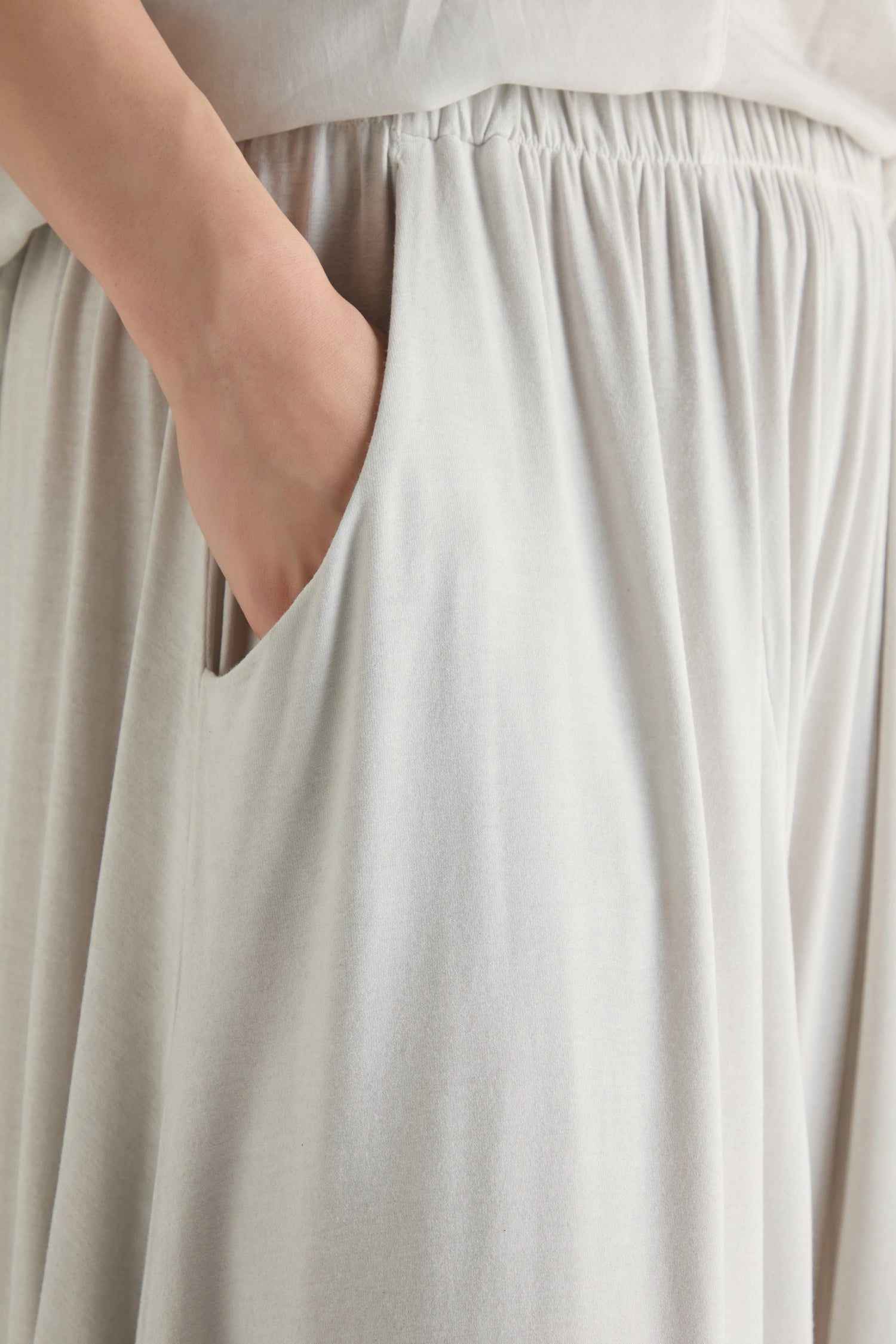 Close-up of a person wearing Soft Drape Jersey Trousers in a light color, featuring a relaxed fit and wide leg style, with their hand casually inside the side pocket.