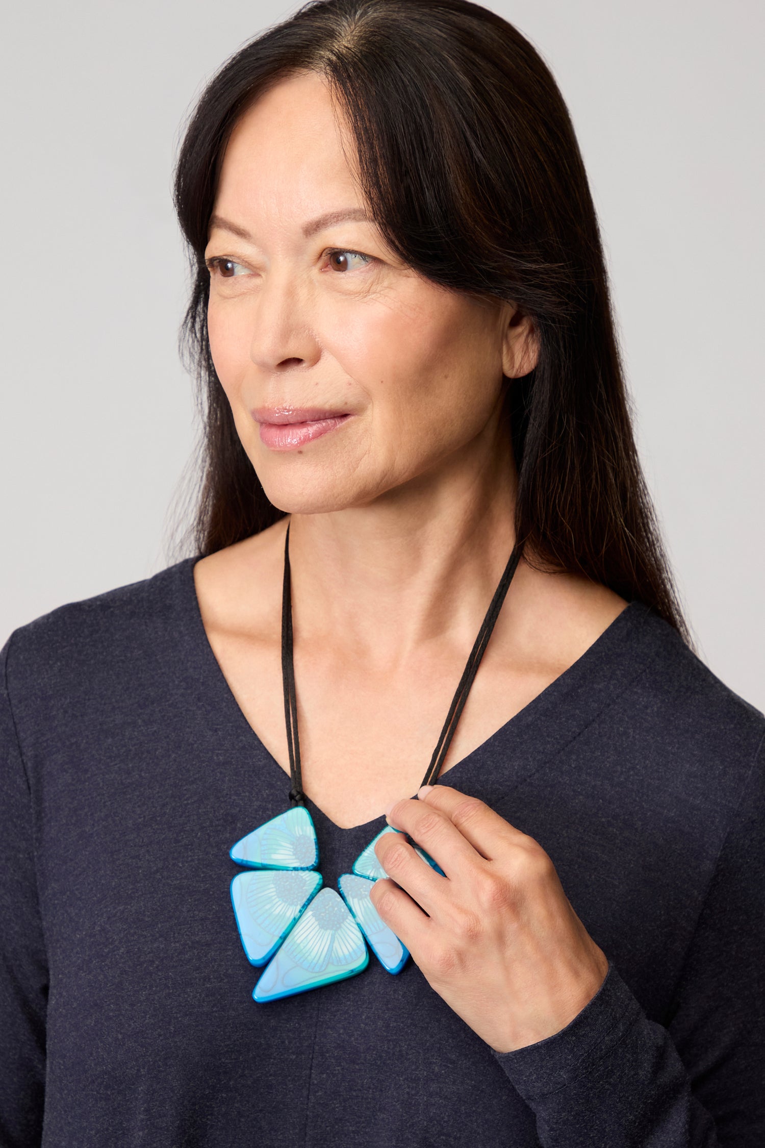 A woman with long dark hair wearing a navy top and the Primula Resin Necklace, featuring bold large blue geometric pieces, looking slightly to the side.