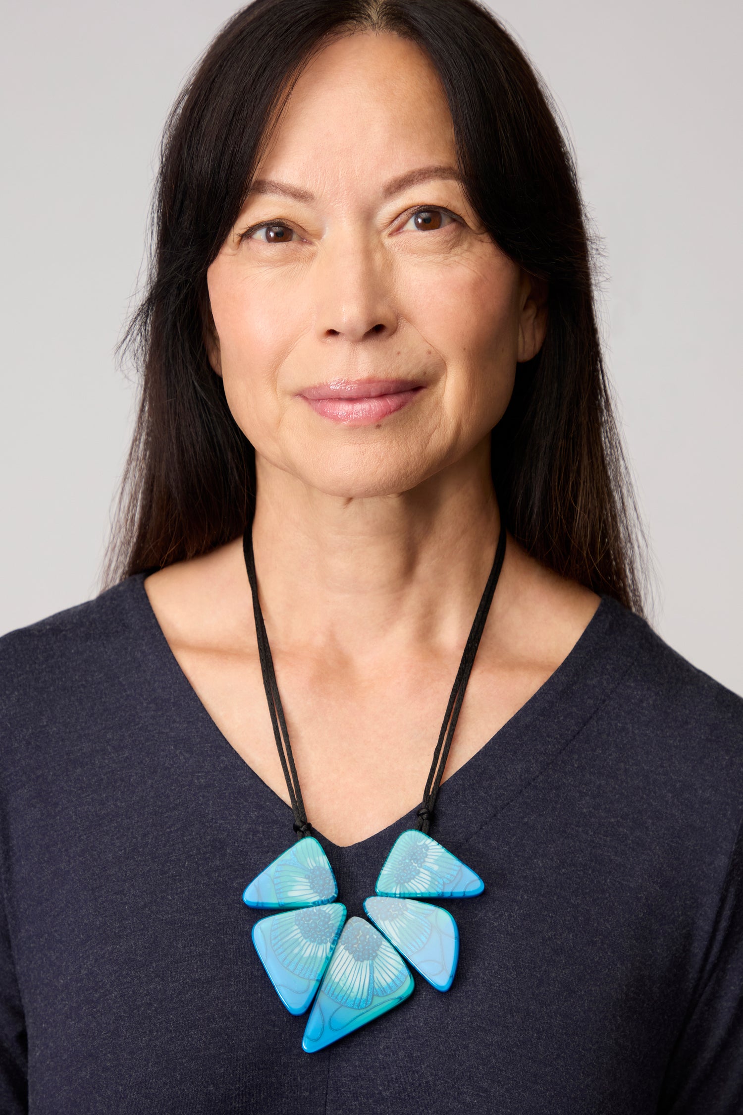 Woman with long dark hair wears a navy top and the Primula Resin Necklace, featuring bold blue resin, looking at the camera with a neutral expression.