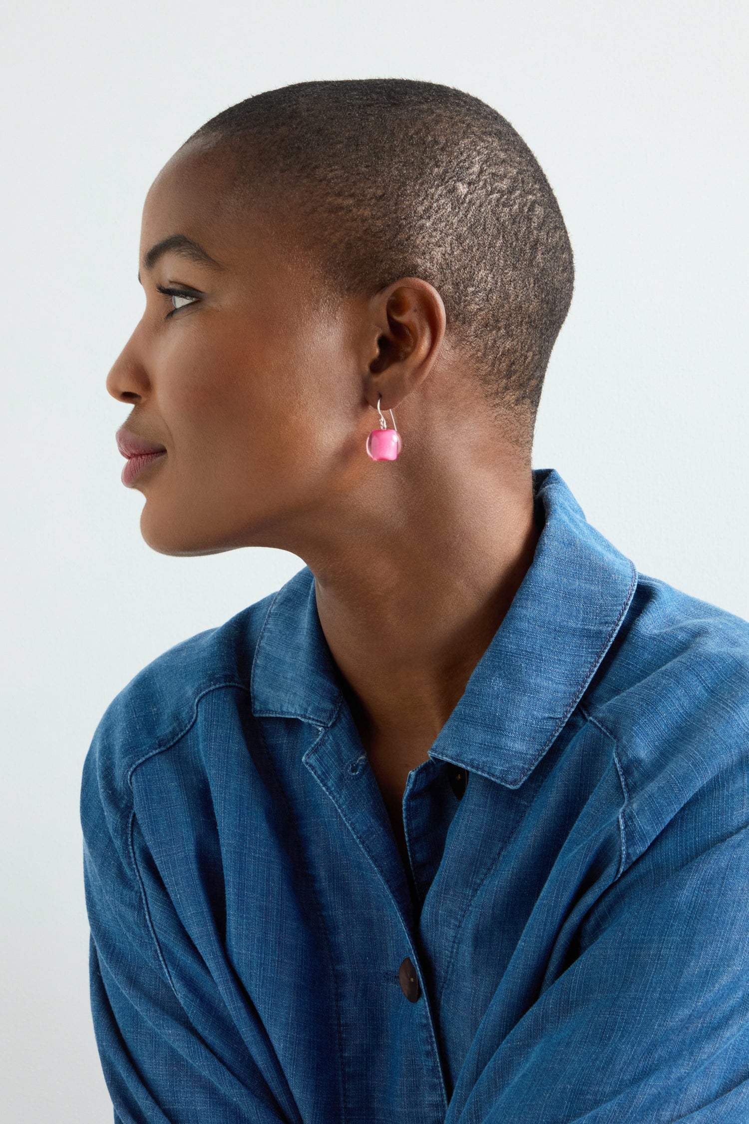 A person with a shaved head is wearing a blue jacket and pink Colourful Bead Earrings, looking to the side.
