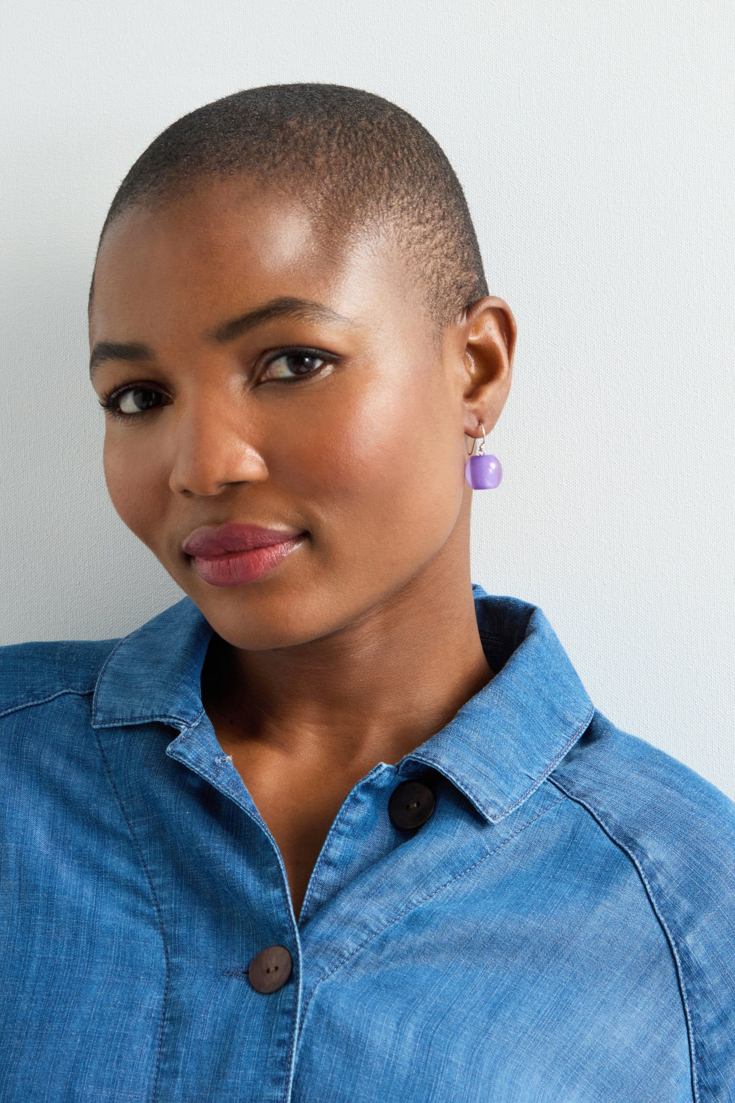 A person in a denim shirt wears vibrant Colourful Bead Earrings, posing against a light-colored background.