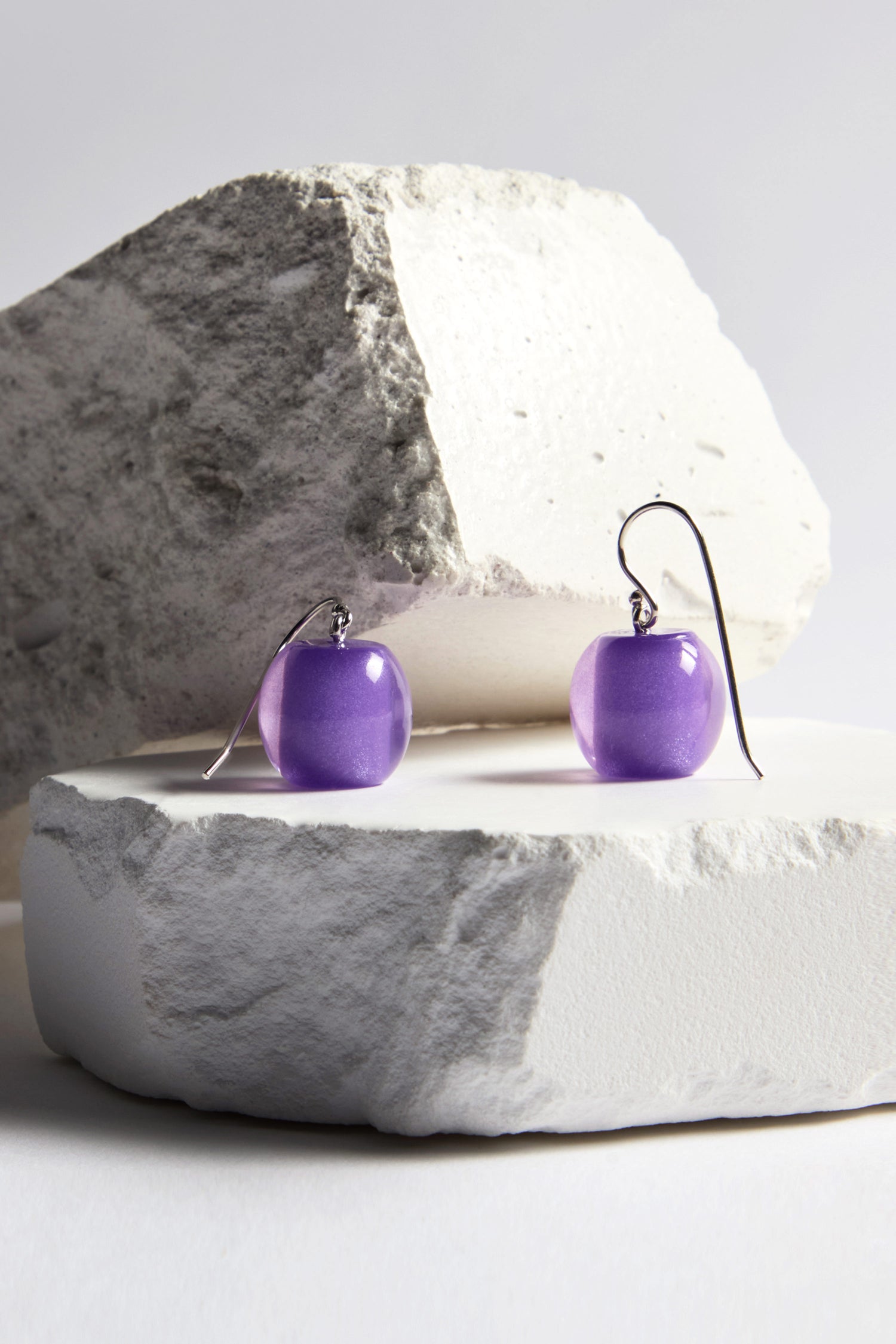 These purple spherical earrings with silver hooks from the Bellisima Collection are elegantly showcased on white stone blocks, enhancing the allure of the Colourful Bead Earrings.