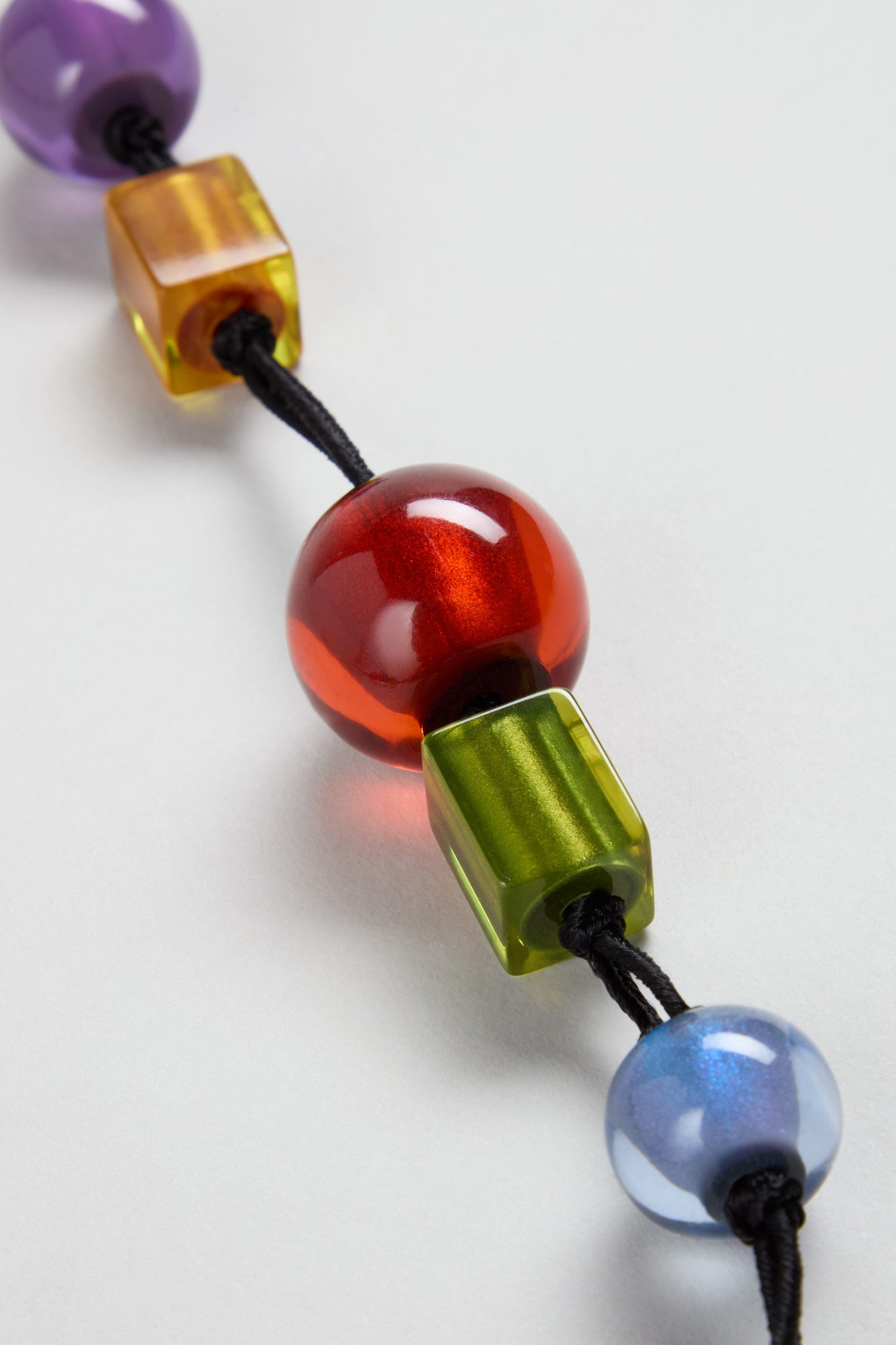 A close-up of the Colourful Shapes Resin Necklace—a black cord strung with shiny round and square resin beads in red, green, blue, purple, and gold—perfect as a handmade statement jewelry piece.